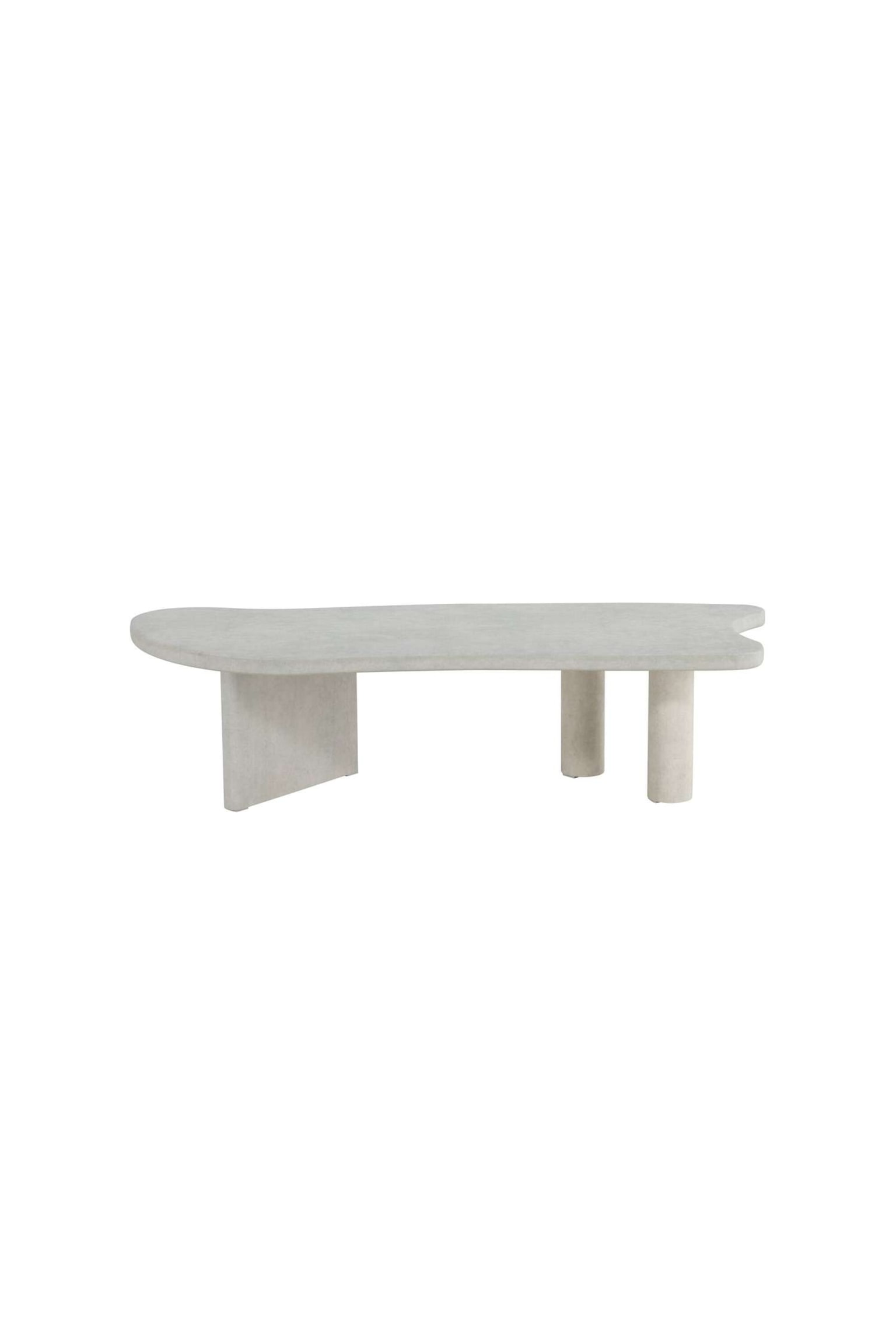 Une table basse gris clair présente un plateau allongé, de forme organique, avec des extrémités arrondies et un côté courbé et irrégulier. Le plateau repose sur un pied en dalle inclinée à gauche et deux pieds cylindriques à droite. - 1