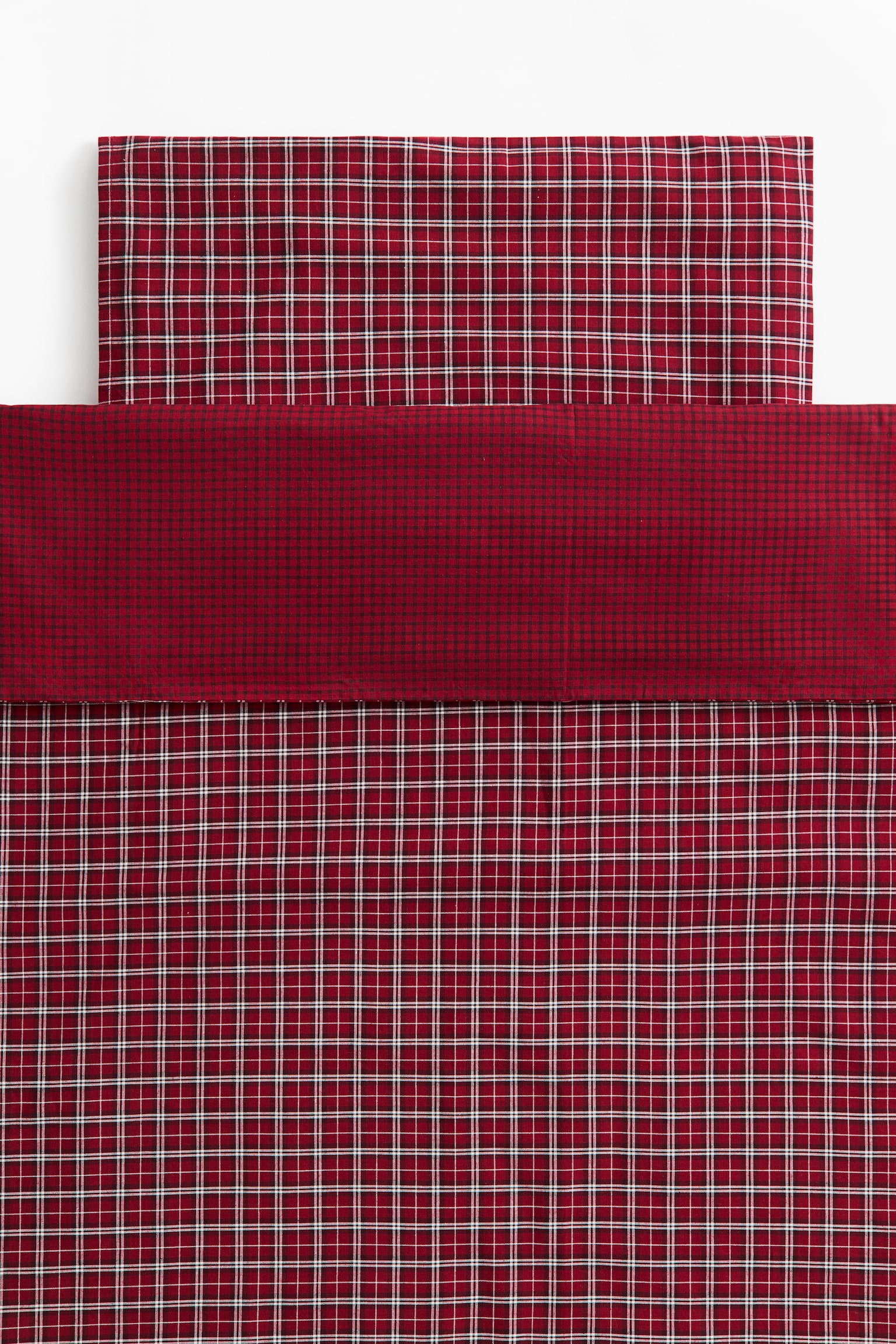 Een rood geruit beddengoedset toont een bijpassende dekbedovertrek en kussensloop, plat uitgespreid. De dekbedovertrek heeft een omgeslagen bovenstuk in een fijn micro-rasterpatroon in donkerrood en zwart, terwijl het hoofdgedeelte en de kussensloop een rood, wit en zwart geruit rasterpatroon tonen.
