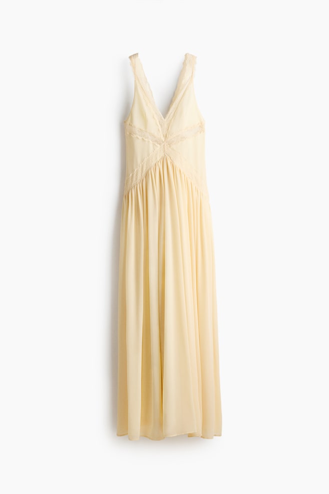 Bleekgele maxi slipjurk met een V-halslijn en delicate kanten afwerking op de bandjes en het lijfje. Het kant vormt een kruispatroon over het voorlijfje, waardoor een empire taille wordt gedefinieerd waaruit de vloeiende rok zich verzamelt. - 1