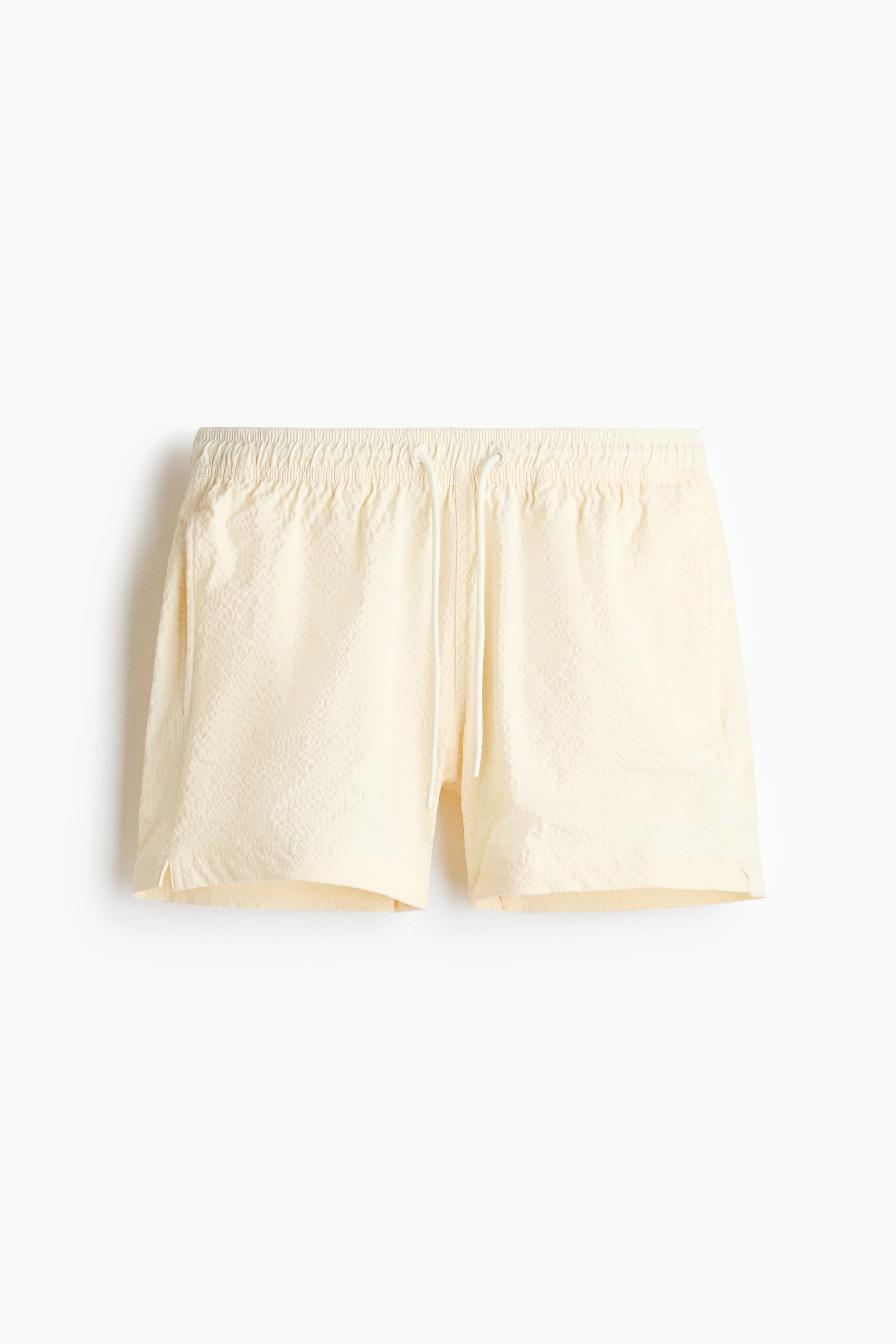 View larger image: Light yellow seersucker swim shorts are displayed front-facing, showcasing a covered elasticated waistband with a white drawstring and small slits at each side of the hem.