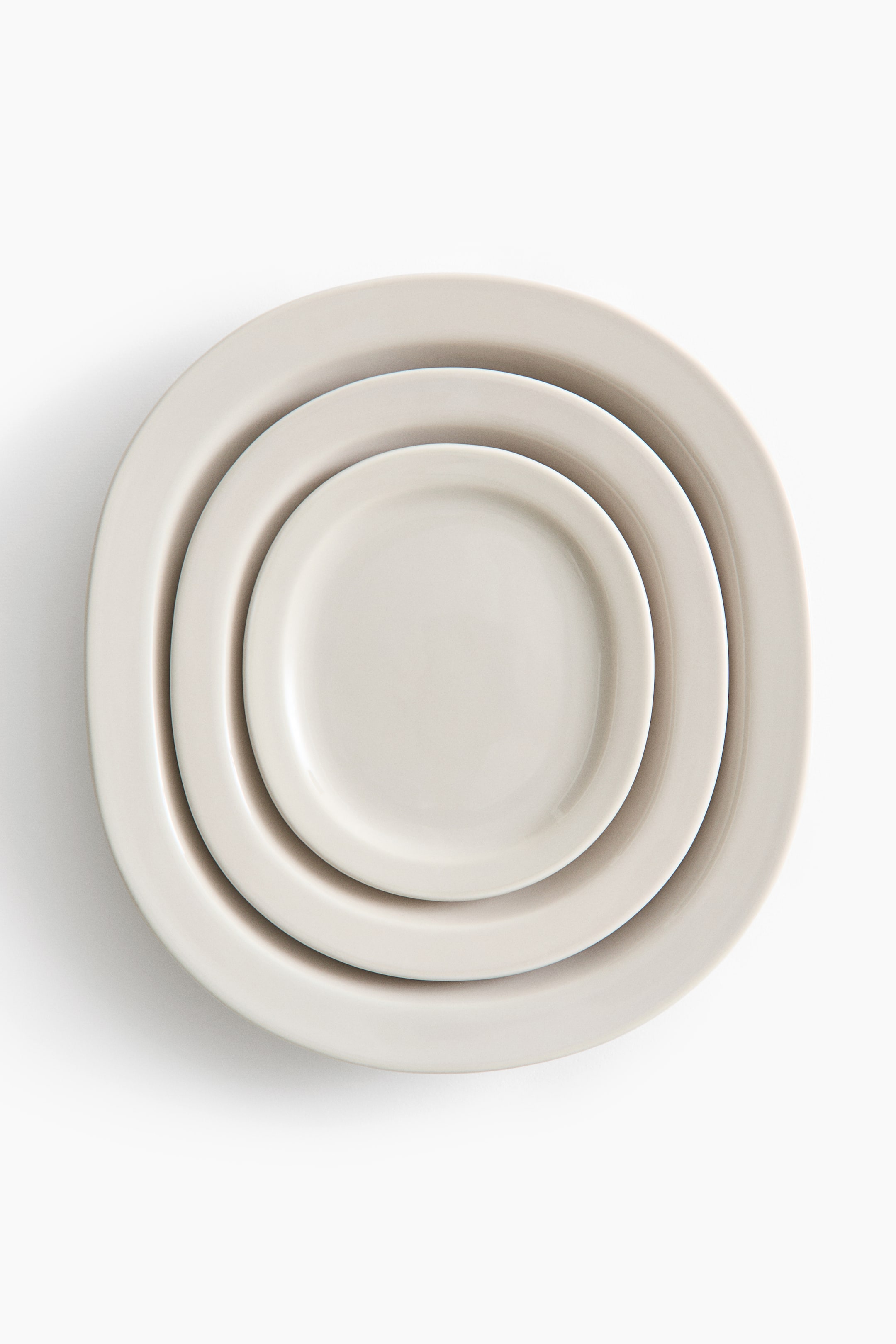 View larger image: Three light beige plates are nested together, each featuring a gently curved rectangular shape with a subtle rim. They vary in size, with the smallest plate fitting neatly inside the larger ones.