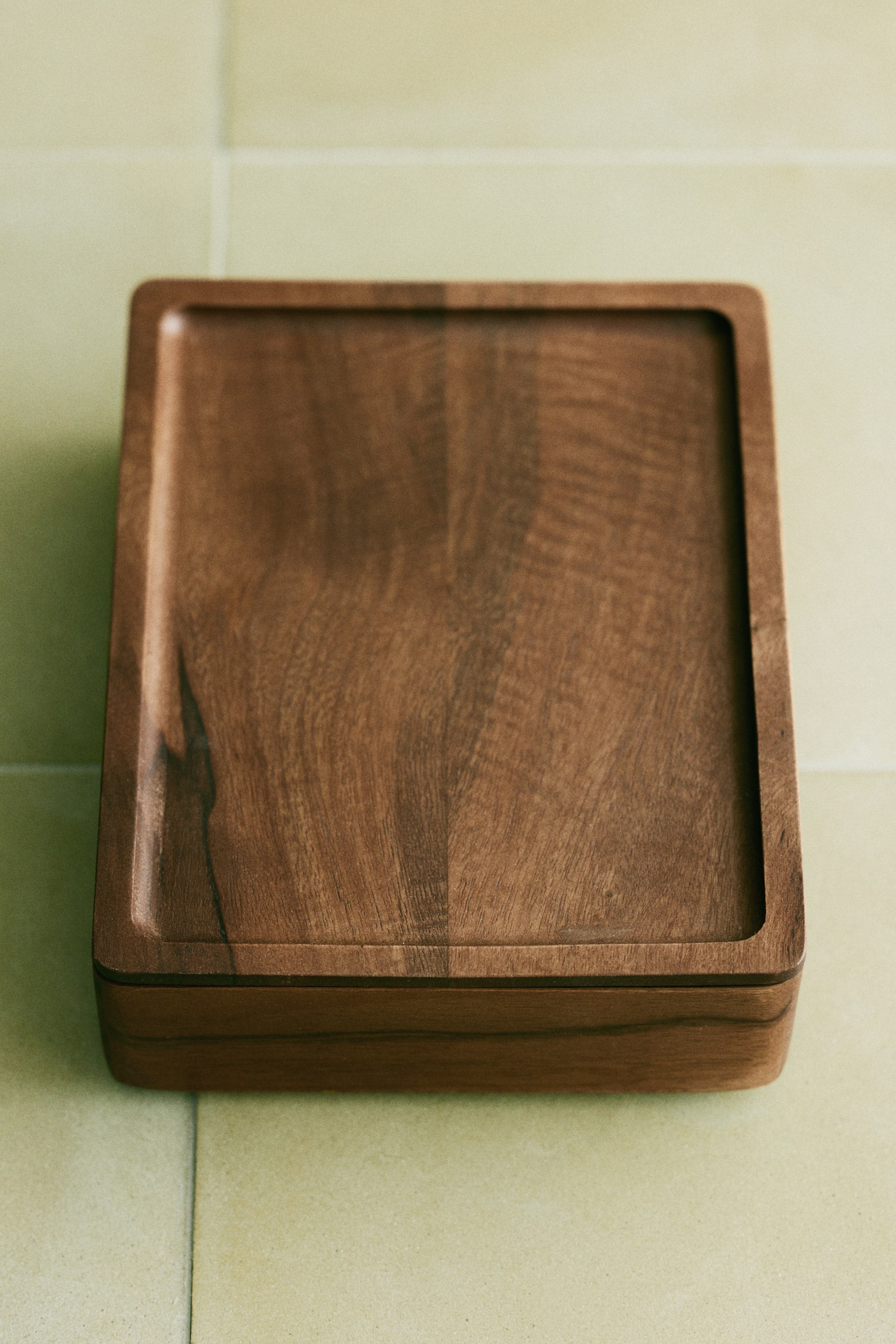 Se større billede: En firkantet trækasse med låg viser en rig træstruktur og afrundede hjørner. Låget har en diskret fordybning på sin øverste overflade.