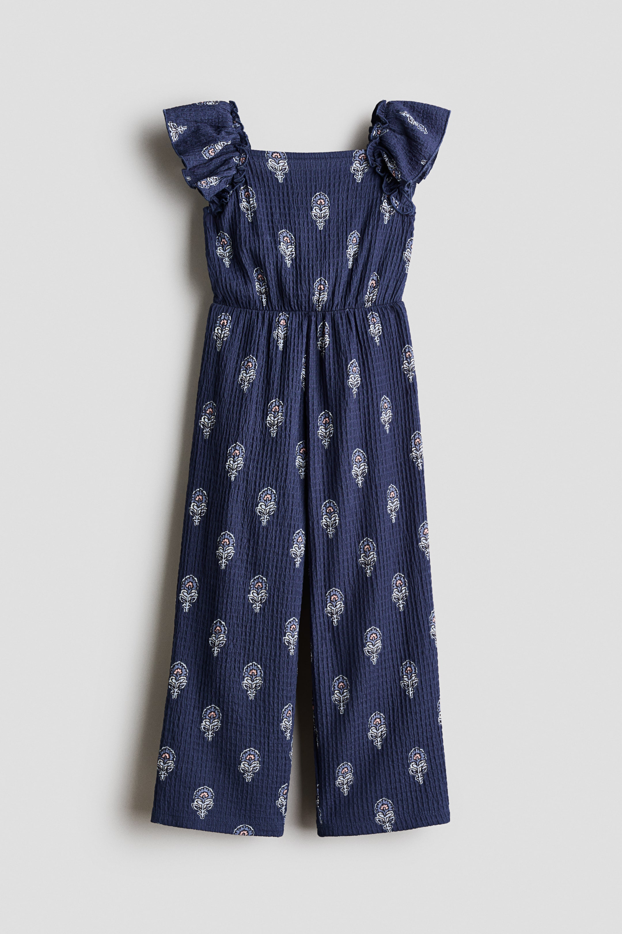View larger image: A dark blue textured jersey jumpsuit, shown from the front, features a white and pink floral pattern throughout. It is designed with a square neckline, flutter sleeves, narrow elastic at the waist, and straight legs.