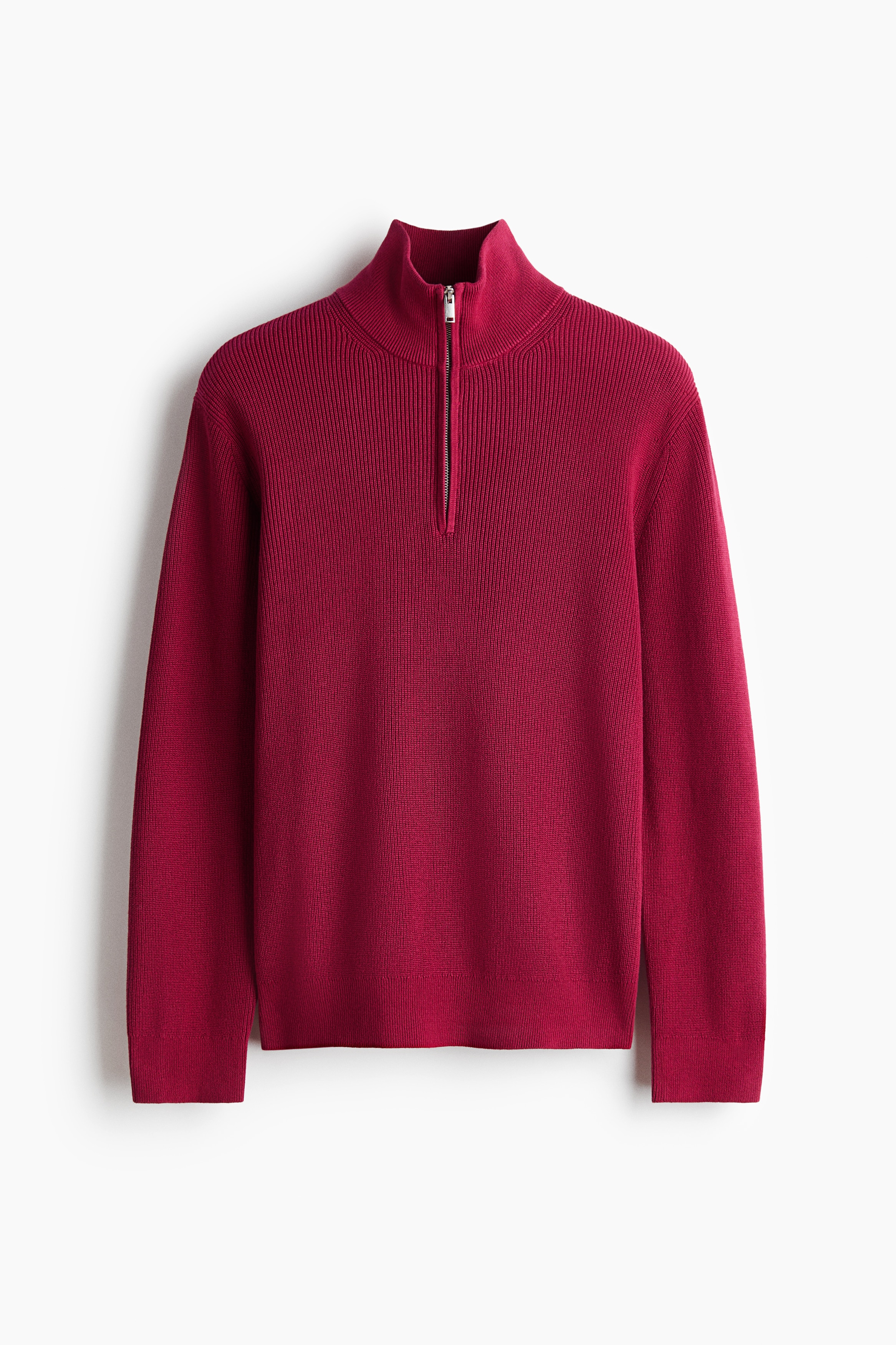 A red, rib-knit cotton sweater featuring a stand collar with an open half-zip is being worn by the model with arms crossed. The sweater is layered over a white crew-neck T-shirt and paired with dark denim jeans.