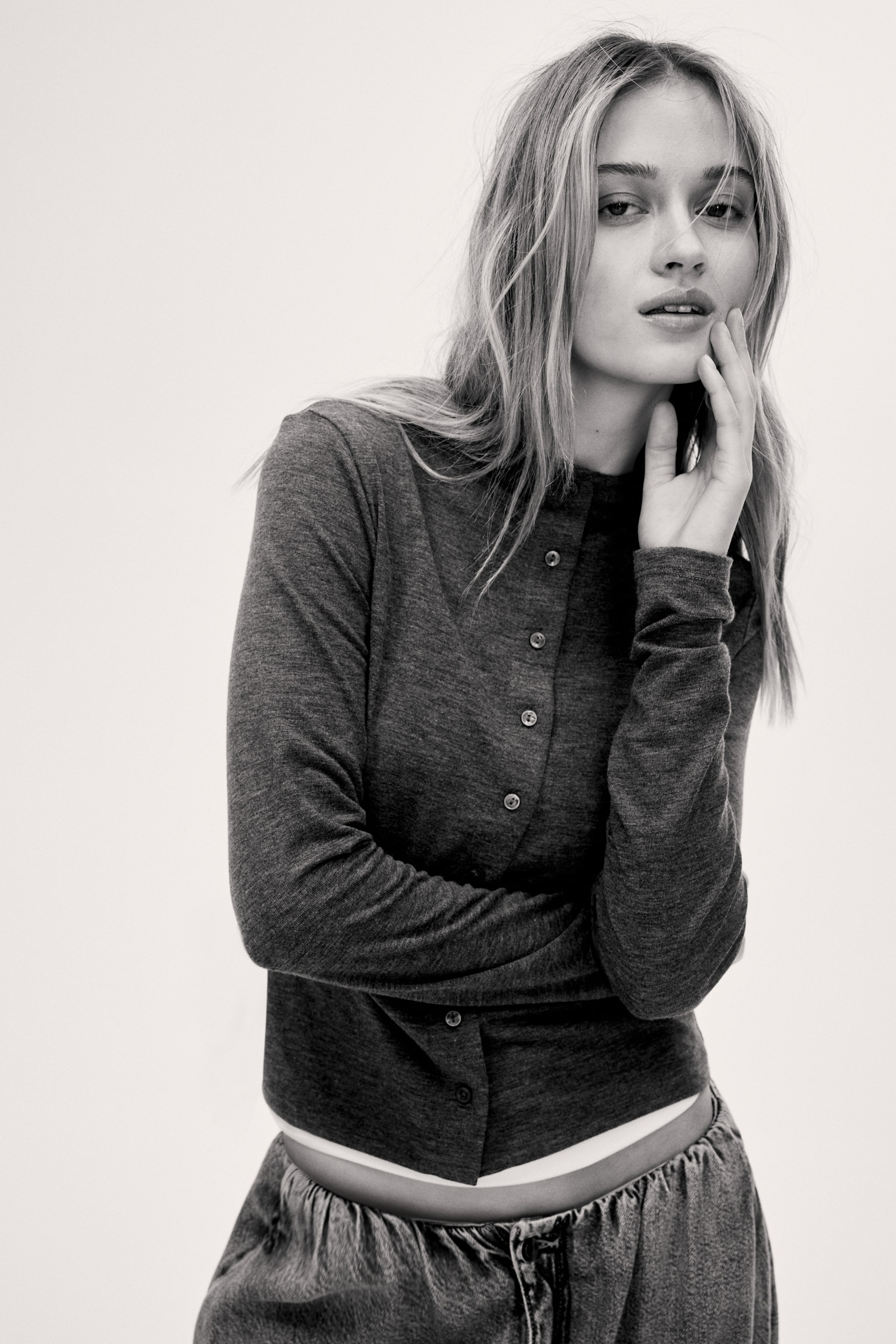 View larger image: A dark grey fine-knit long-sleeved top is facing forward, featuring a band collar and a full front button placket with light-coloured round buttons. Its cropped hem is exposing a white layer underneath.