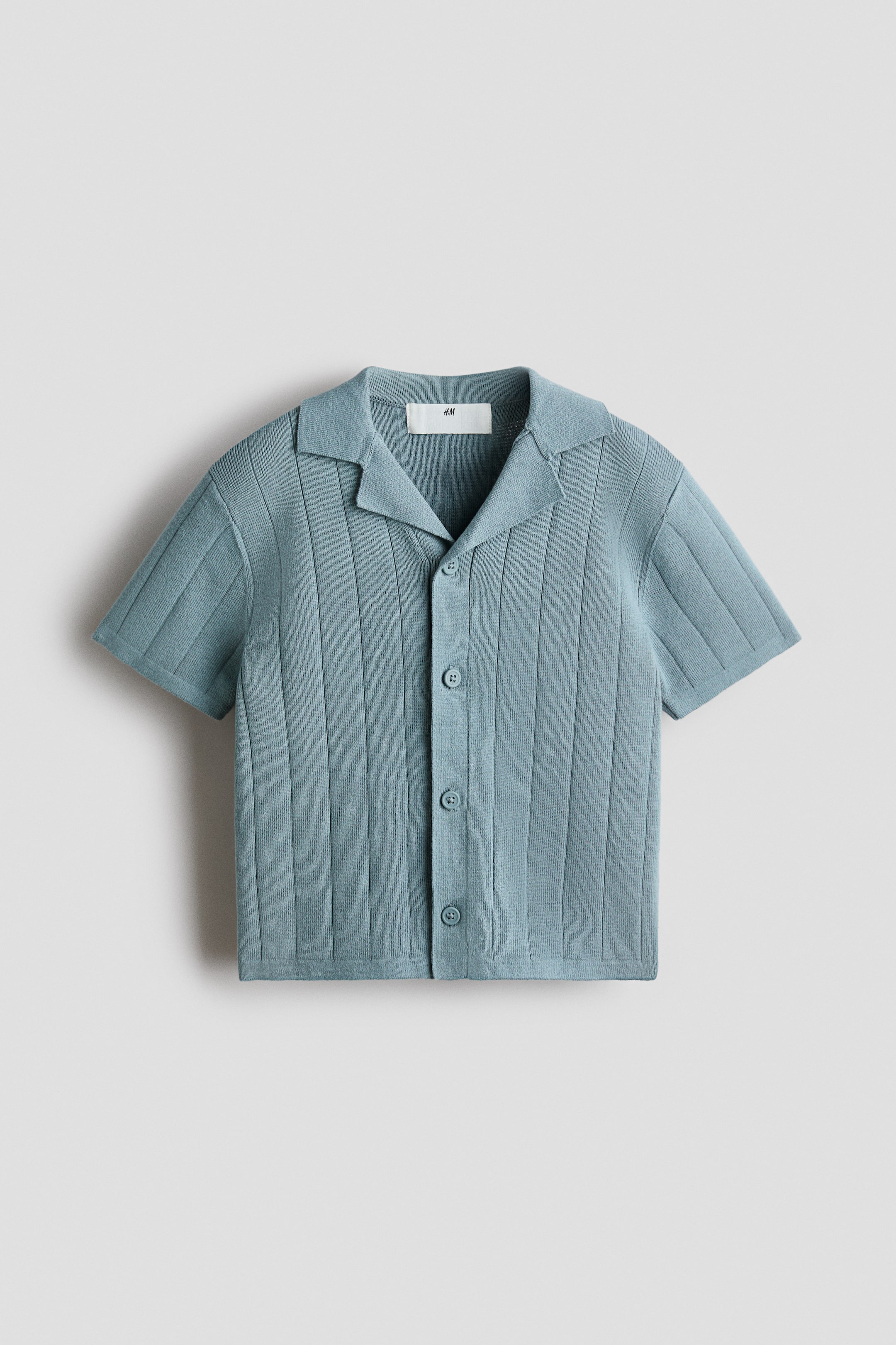 View larger image: The light blue-green knitted short-sleeved shirt showcases a ribbed texture across its body and sleeves. It features an open collar and a full button placket with five round buttons at the front.