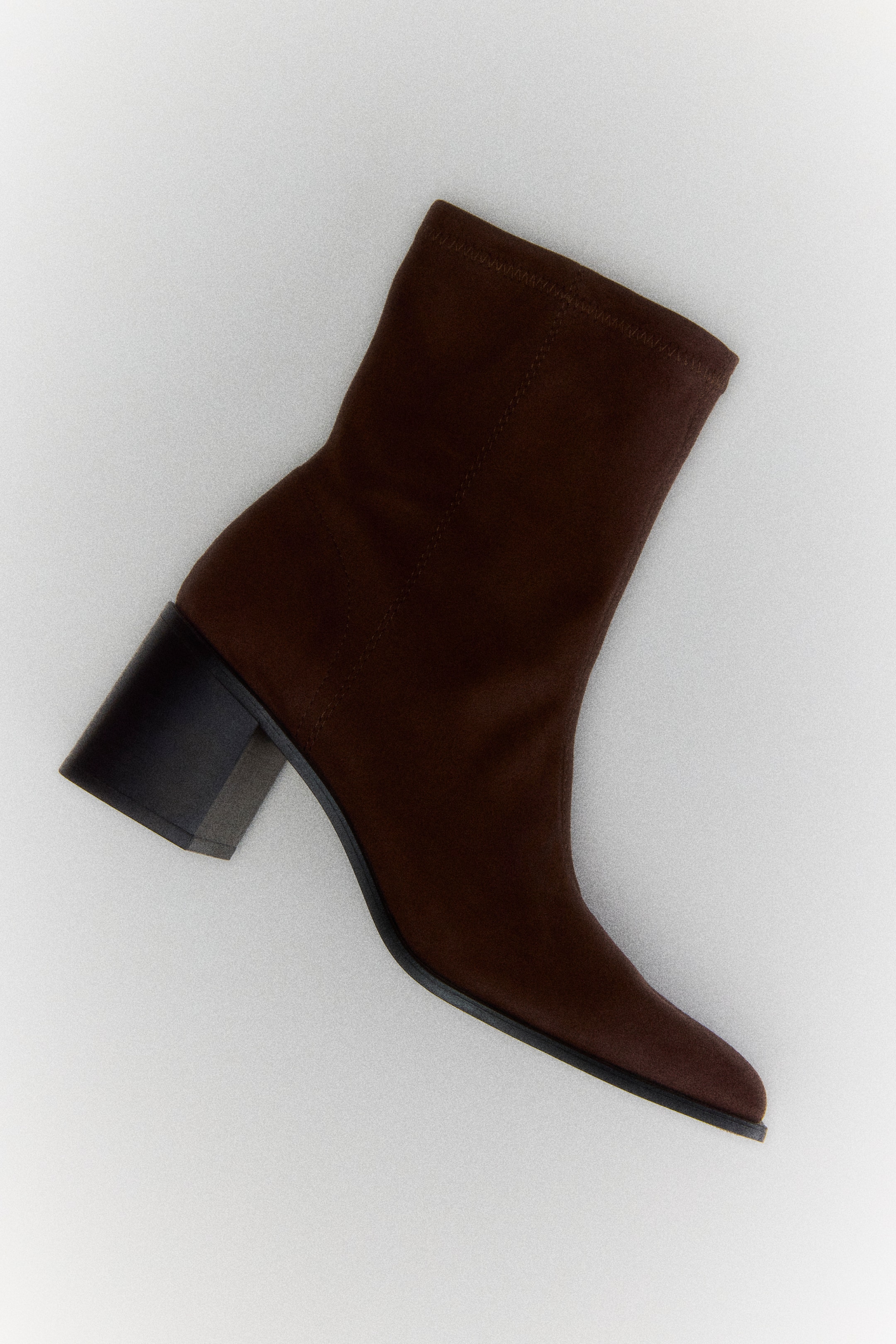 View larger image: A dark brown ankle boot is shown in a side profile view, featuring a stretchy suede-like shaft, a chisel toe, and a contrasting black block heel.