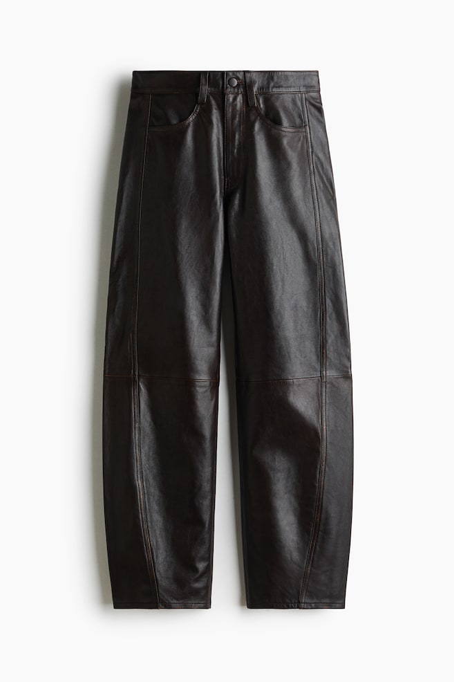 A pair of dark brown leather trousers is shown front-facing, displaying a wide-leg silhouette with distinctive curved panel detailing and horizontal seam details across the knees. The trousers feature a structured waistband with belt loops, a classic five-pocket design, and a button-fly closure. - 1