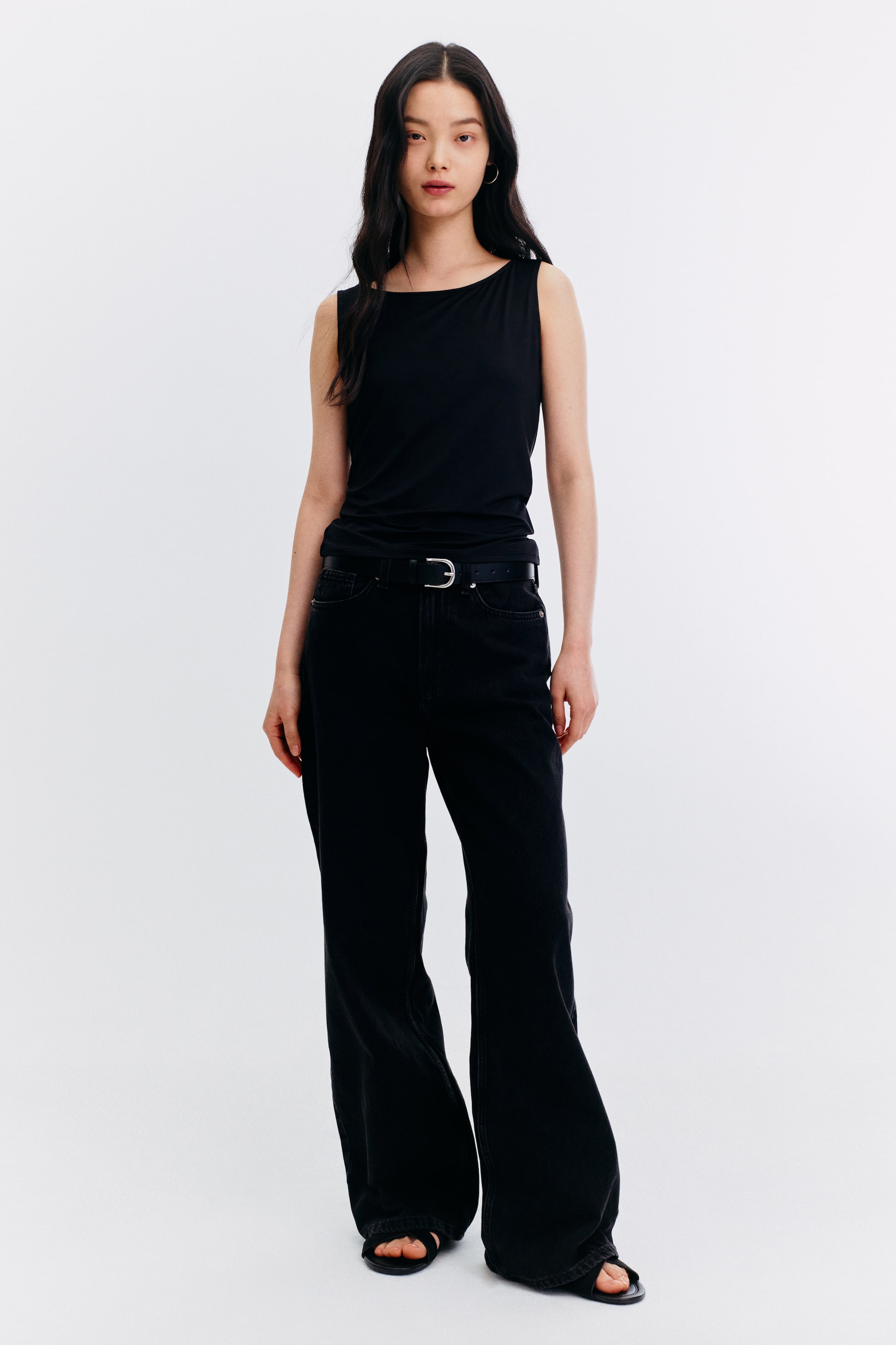 View larger image: The model is wearing a black sleeveless top, showcasing a boat neck and a fitted silhouette, neatly tucked into black wide-leg jeans.