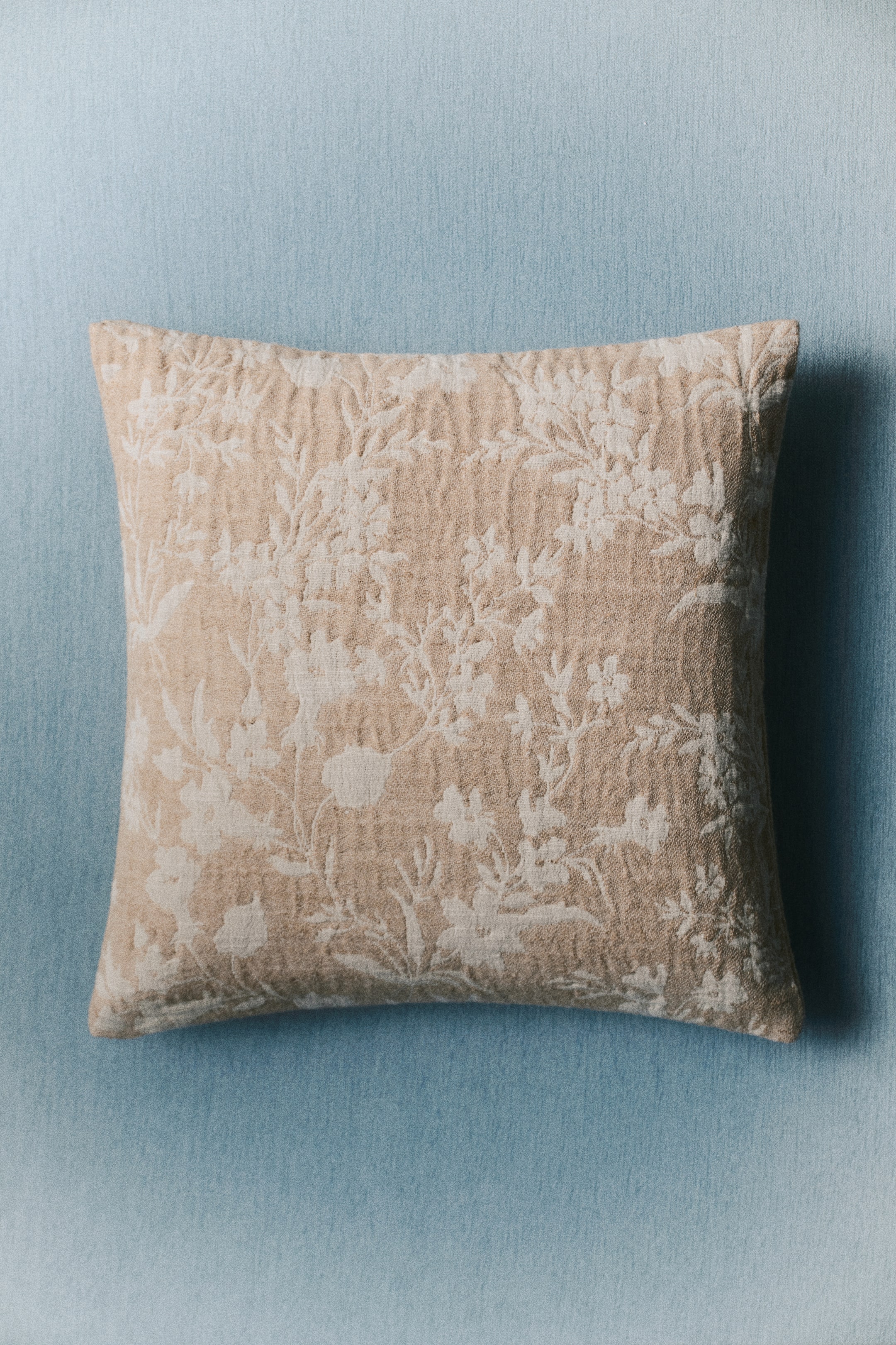 View larger image: A cushion cover is lying flat, showcasing its front side adorned with a botanical pattern in a textured jute-blend jacquard weave.