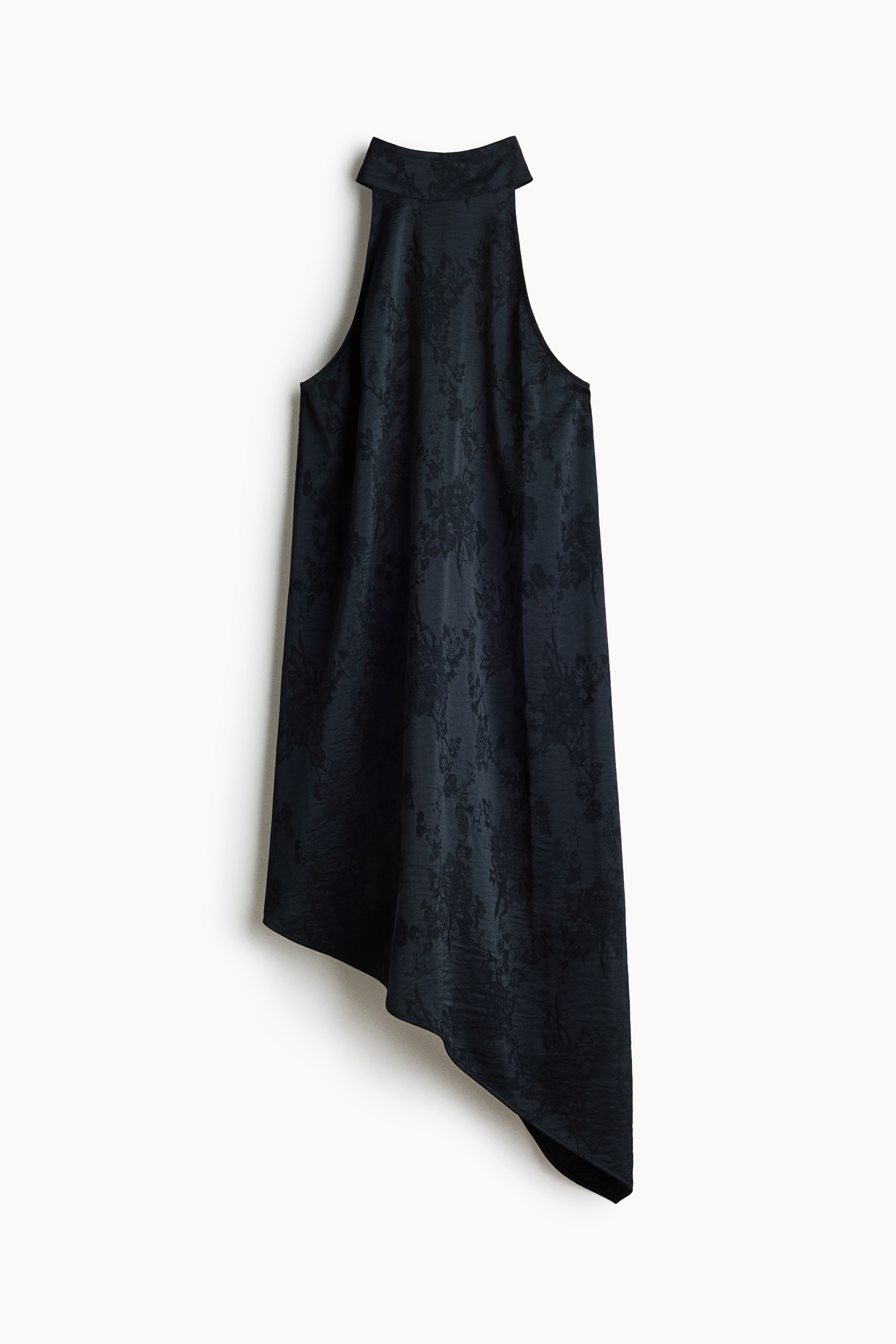 The model is wearing a black sleeveless dress in a textured floral jacquard weave. The dress features a high stand collar with a halter-style neckline and a relaxed silhouette that ends in an asymmetrical hem.