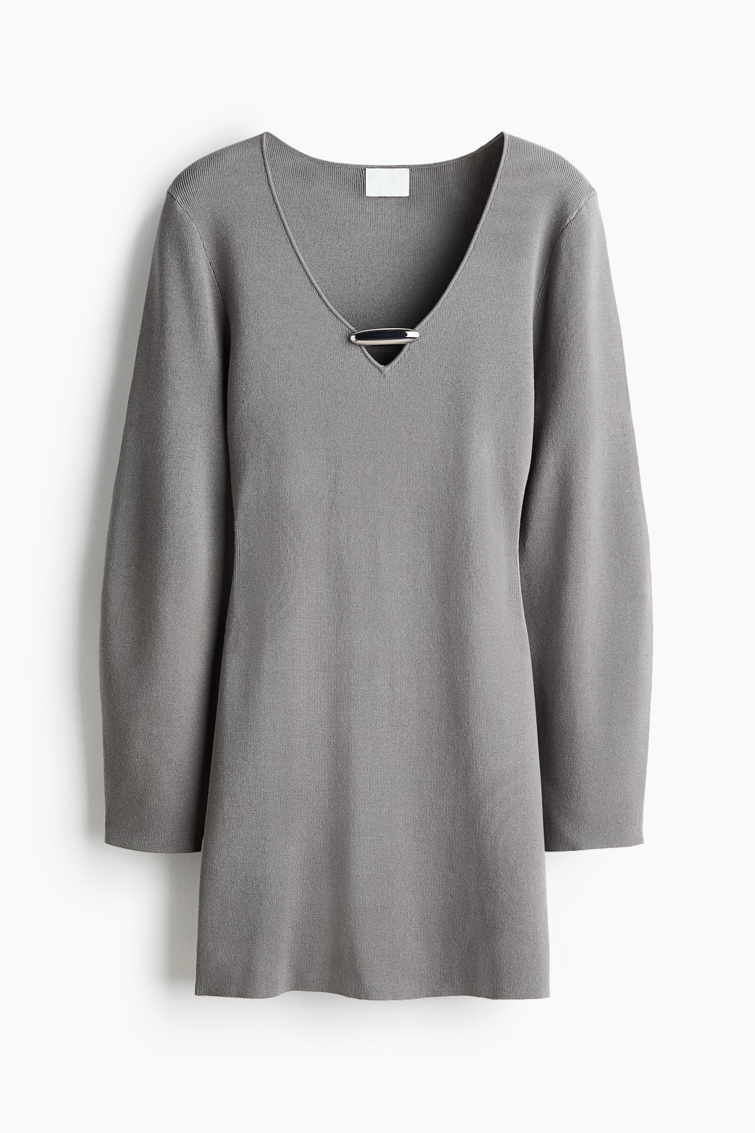 Cette mini-robe en tricot grise est présentée de face, avec un profond décolleté en V rehaussé par une barre métallique horizontale ton argent. La robe met en valeur de longues manches légèrement amples ainsi qu’une silhouette droite dans une texture en maille fine.