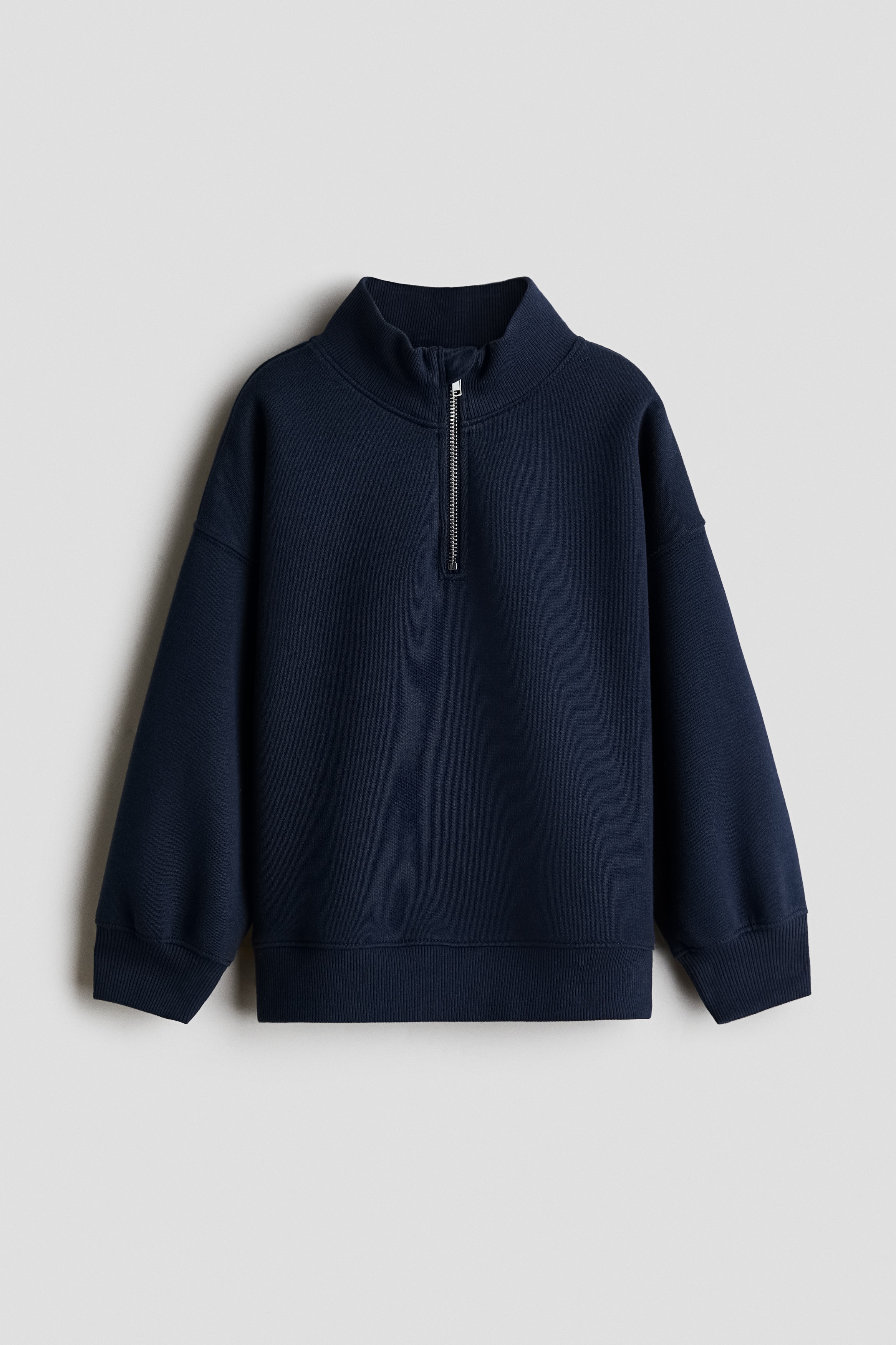 Má»t chiáº¿c Ã¡o len ná» cháº£i mÃ u xanh navy ÄÆ°á»£c chá»¥p tá»« phÃ­a trÆ°á»c, ná»i báº­t vá»i cá» Äá»©ng cÃ³ khÃ³a kÃ©o ná»­a mÃ u báº¡c, vai trá» vÃ  tay dÃ i. Ão len cÃ³ bo tay vÃ  gáº¥u Ã¡o dá»t gÃ¢n, ÄÆ°á»£c phá»i cÃ¹ng Ã¡o lÃ³t mÃ u tráº¯ng.