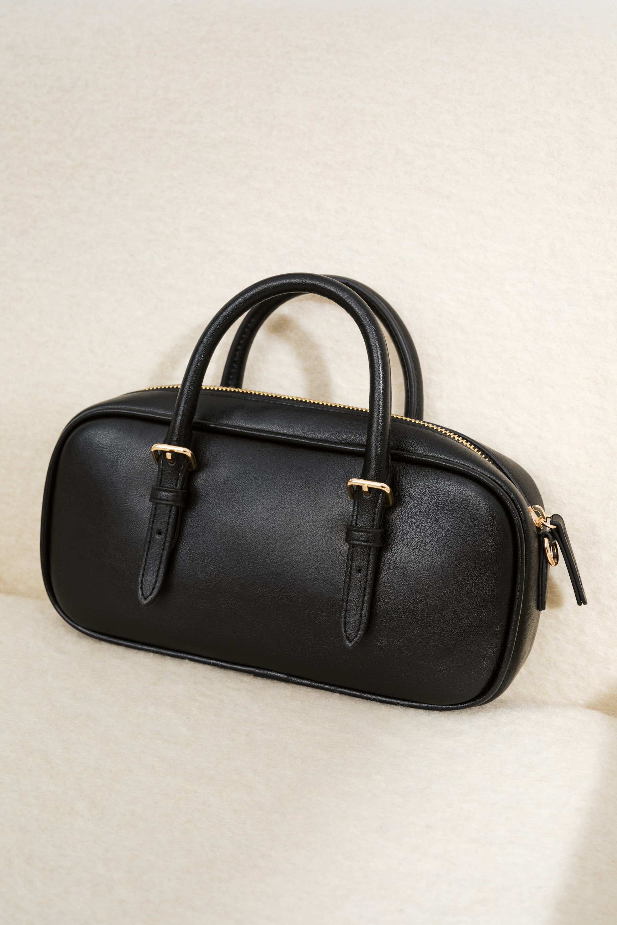 View larger image: A black rectangular crossbody bag is showcased. It features a top zip closure with a gold-toned zipper, and two top handles secured by straps with gold-toned metal buckles.