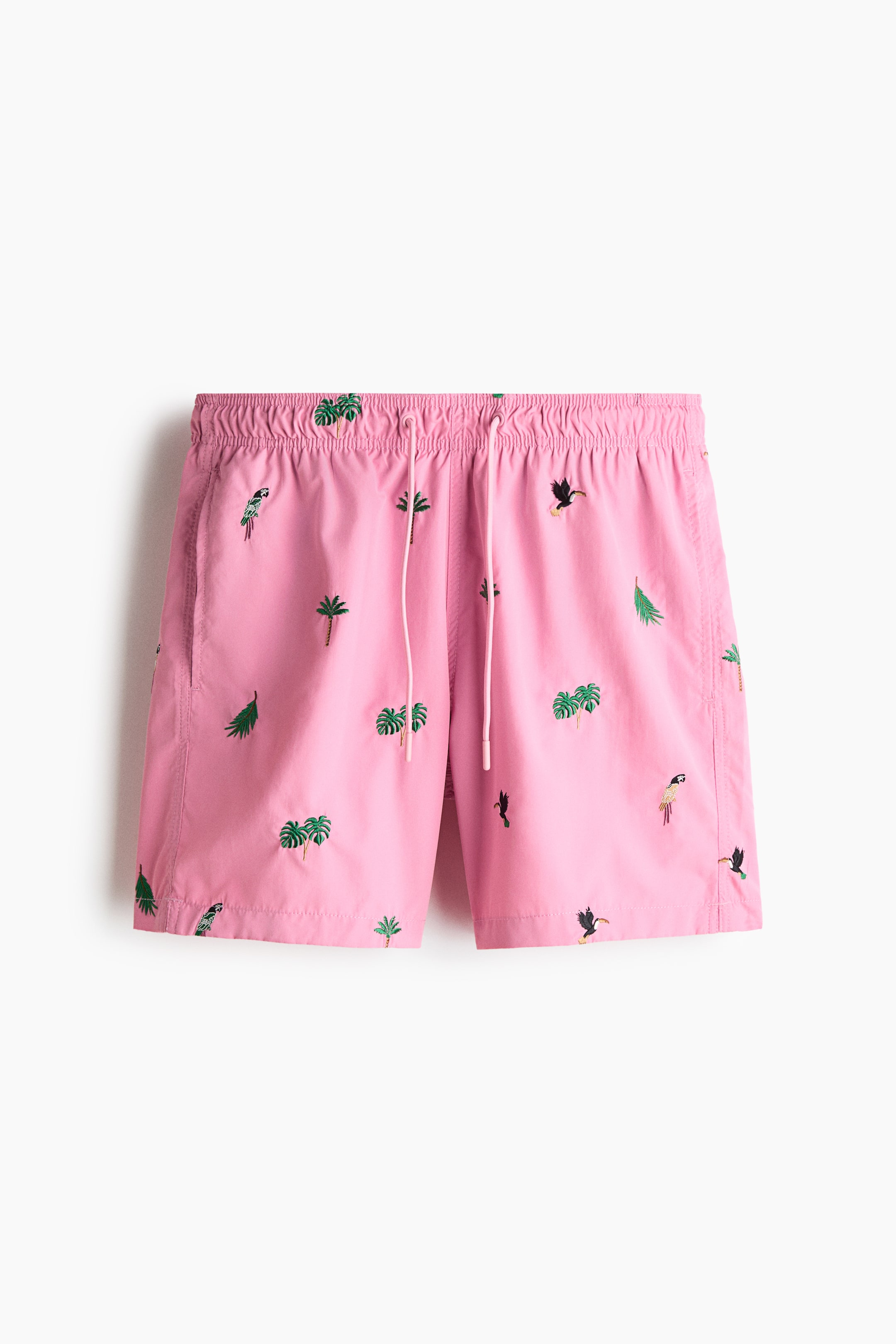 View larger image: Pink shorts showcase an elasticated waistband with a white drawstring and side seam pockets. The shorts feature an all-over embroidery pattern of green palm trees, various green leaves, toucans, and parrots.