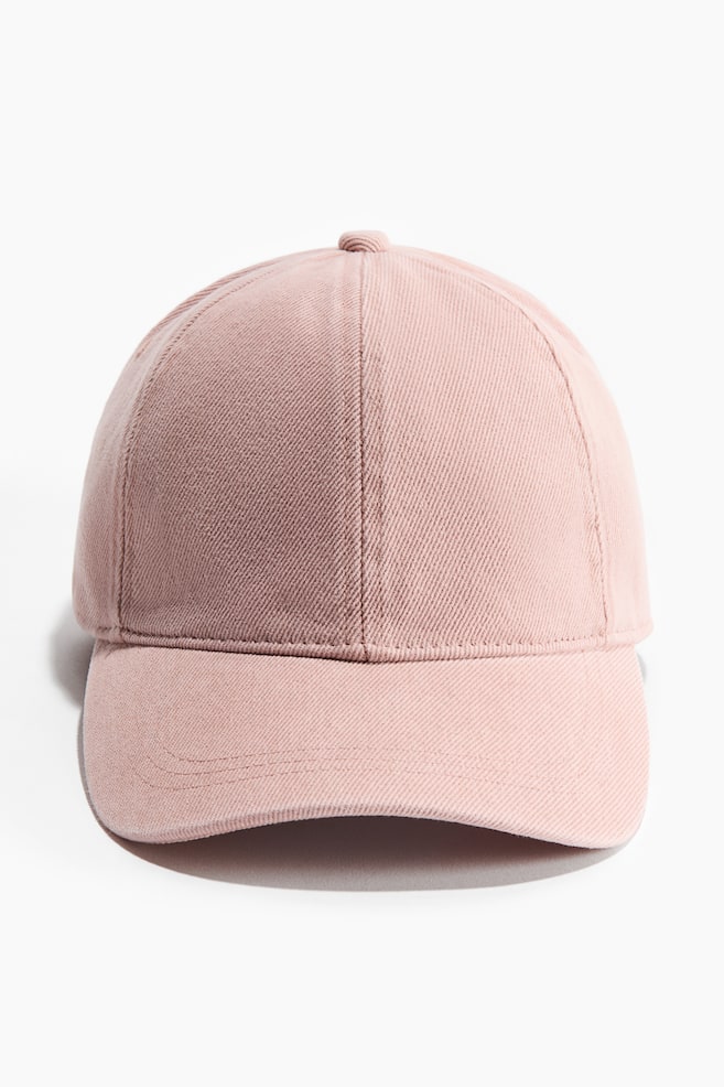 Um boné de basebol rosa é apresentado de frente, com uma coroa de seis painéis com um botão no topo e uma aba curva, tudo construído a partir de um tecido de sarja com linhas diagonais visíveis. - 1