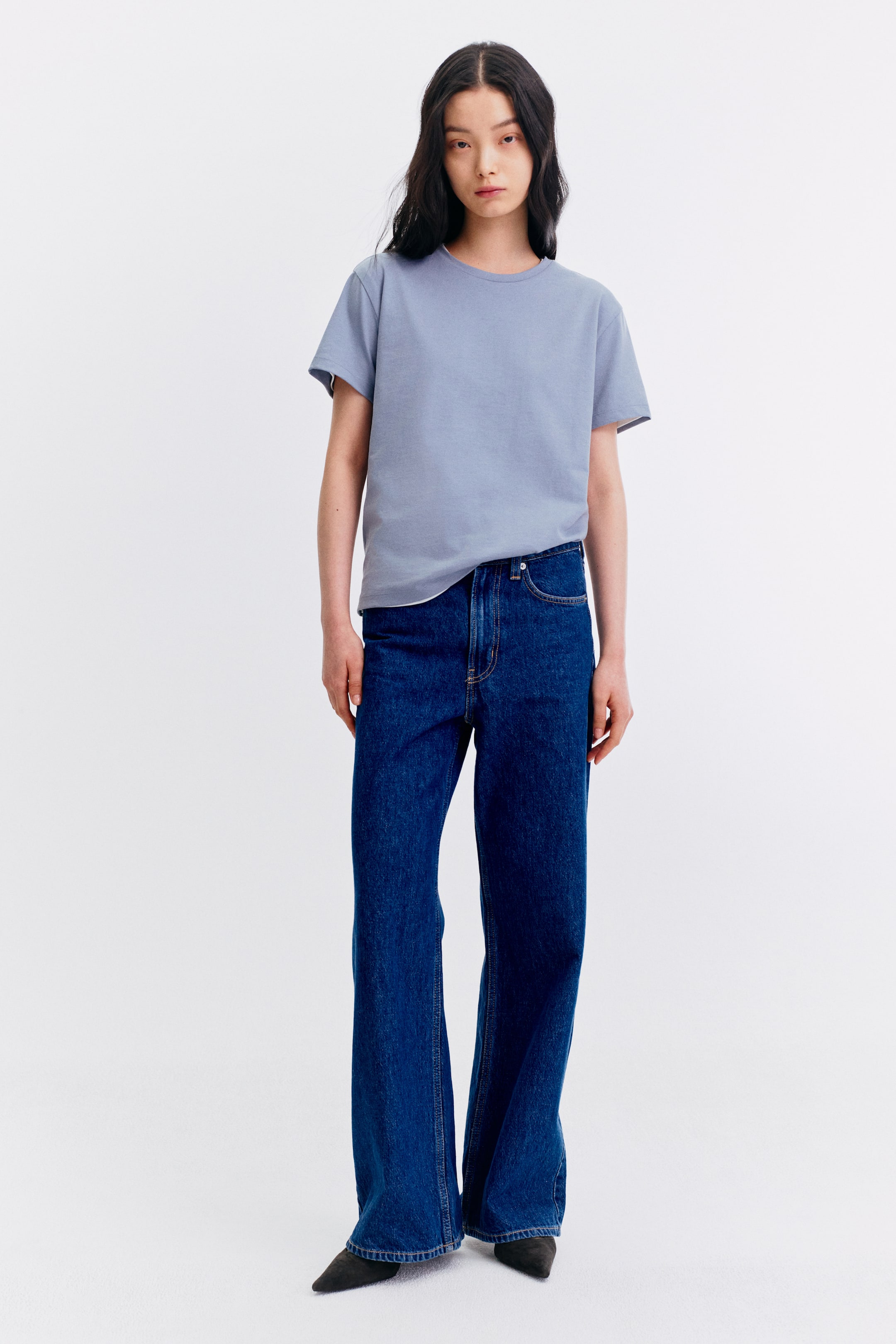 View larger image: The model is showcasing a light blue short-sleeved crew neck tee, partially tucked into dark wash denim jeans.