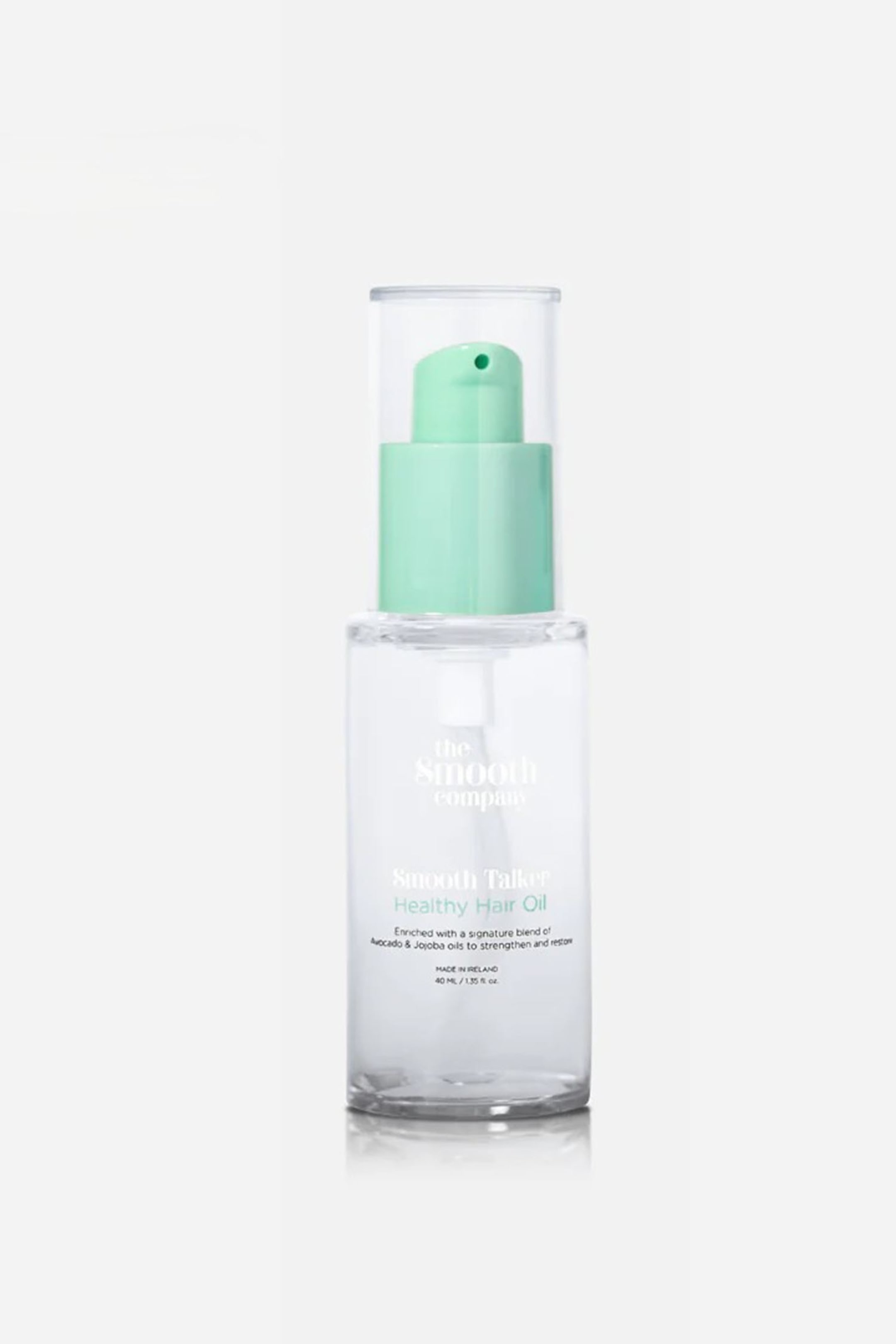 Se større billede: En klar glasflaske med "Smooth Talker Healthy Hair Oil" står oprejst og vender fremad, med en mintgrøn pumpe og en gennemsigtig beskyttelseshætte. Flaskens front viser mærkenavnet "the Smooth company" og yderligere produktinformation.