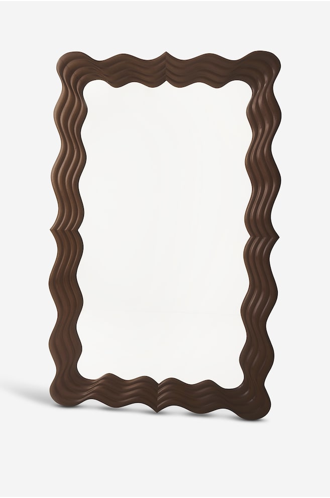 Een rechthoekige spiegel staat iets naar links gekanteld en toont een donkerbruinen houten lijst met een diep gesculpteerd, golvend golfdesign. - 1