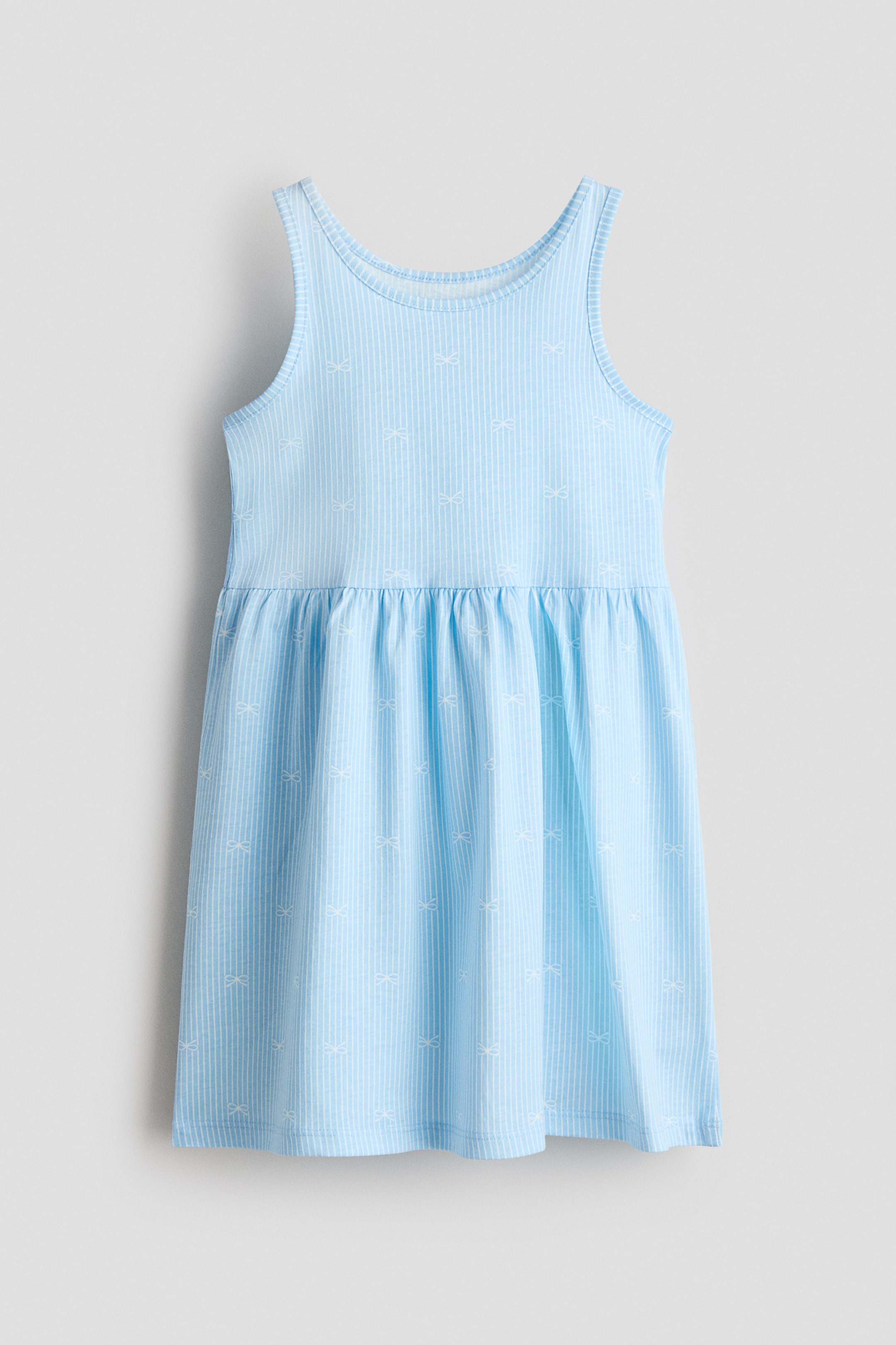 View larger image: Sleeveless dress shown from the front, made from light blue ribbed jersey featuring white vertical stripes and small white bow motifs. It is designed with a gathered seam at the waist and a gently flared skirt.