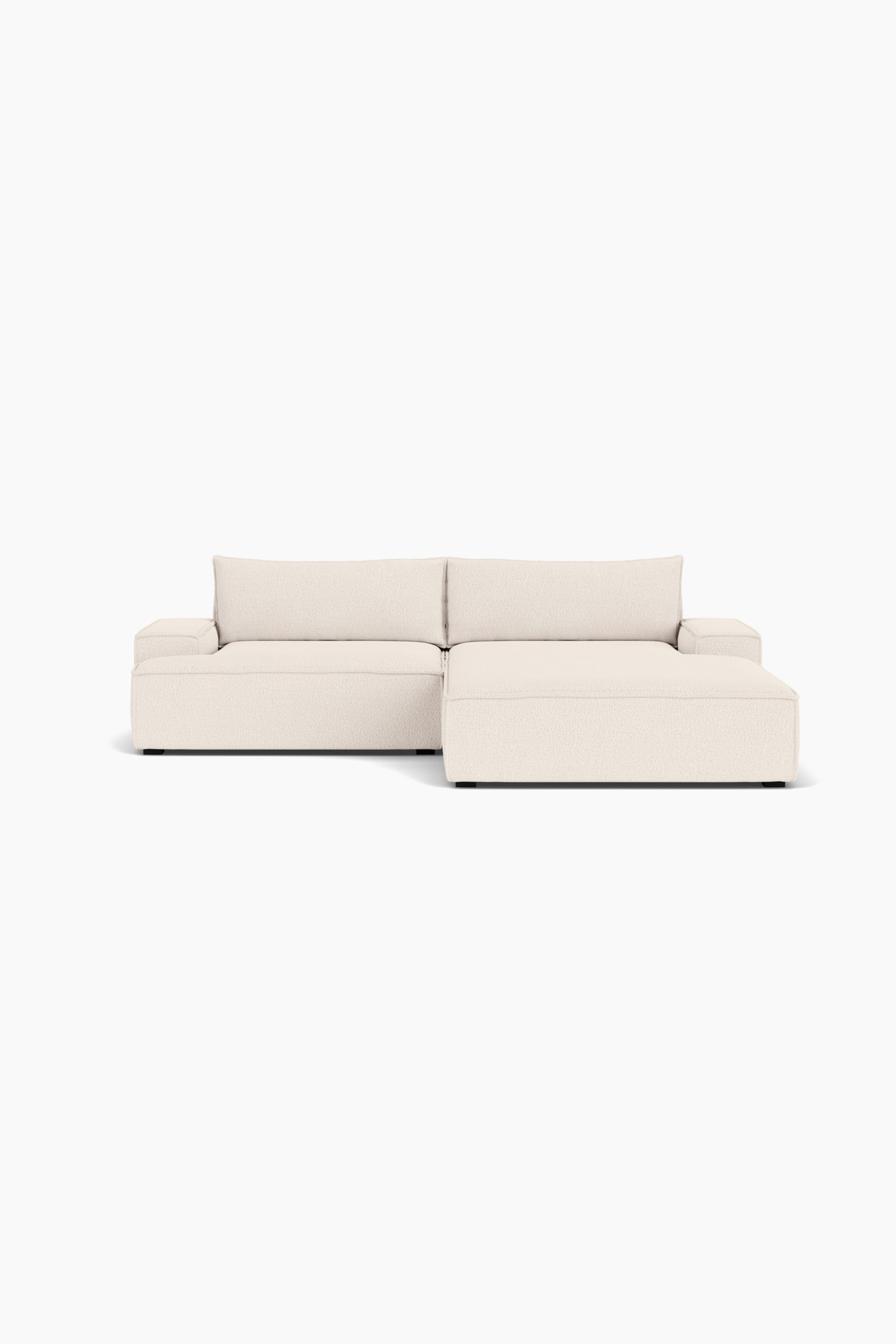 Größeres Bild ansehen: Ein cremefarbenes modulares Ecksofa mit rechtsseitiger Chaise-Lounge ist nach vorne ausgerichtet und präsentiert sein flaches Design sowie den strukturierten Stoffbezug. Das Sofa verfügt über dicke, kantige Sitzkissen, breite, flache Armlehnen und zwei große, passende Rückenkissen.