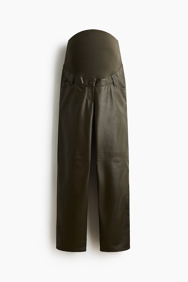 Une paire de pantalons de grossesse vert olive foncé est présentée de face, avec une large ceinture en jersey extensible à porter au-dessus du ventre. Le corps principal est confectionné en faux cuir lisse, affichant une coupe droite avec des poches italiennes sur le devant, des passants de ceinture, une fermeture à un seul bouton et des coutures horizontales au niveau des genoux. - 1