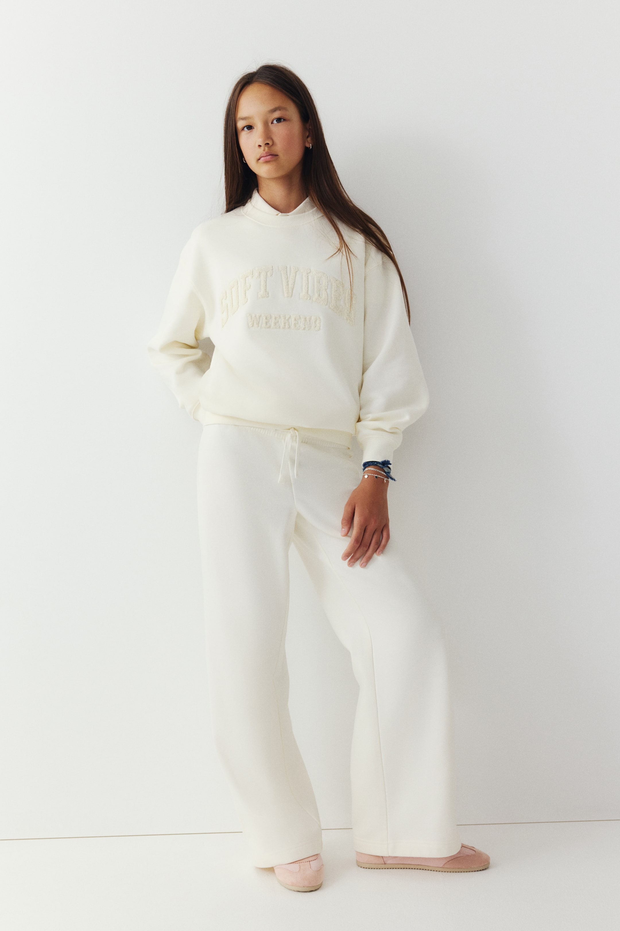 Vis større bilde: Off-white joggebukser vises forfra, med en avslappet passform med rette ben og elastisk linning med snøring. Buksen er stylet med en matchende kremfarget sweatshirt og lyserosa sko.