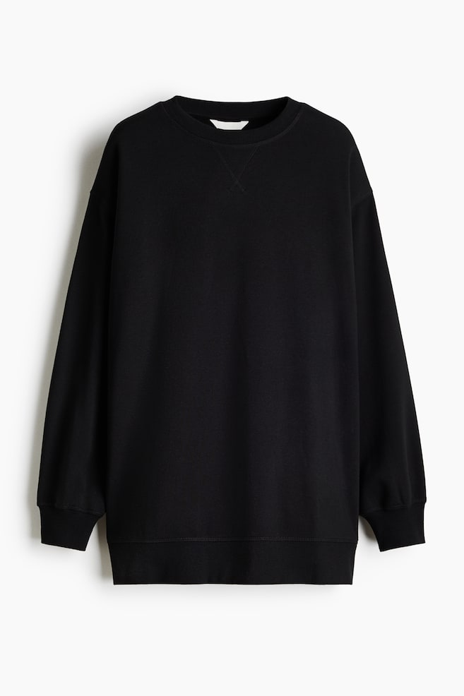 Se muestra una sudadera negra de corte oversize vista de frente, con hombros caÃdos, mangas largas con puños acanalados y un cuello redondo acanalado con el clásico detalle de costura en V. La prenda cuelga recta, mostrando su silueta relajada y el bajo acanalado. - 1