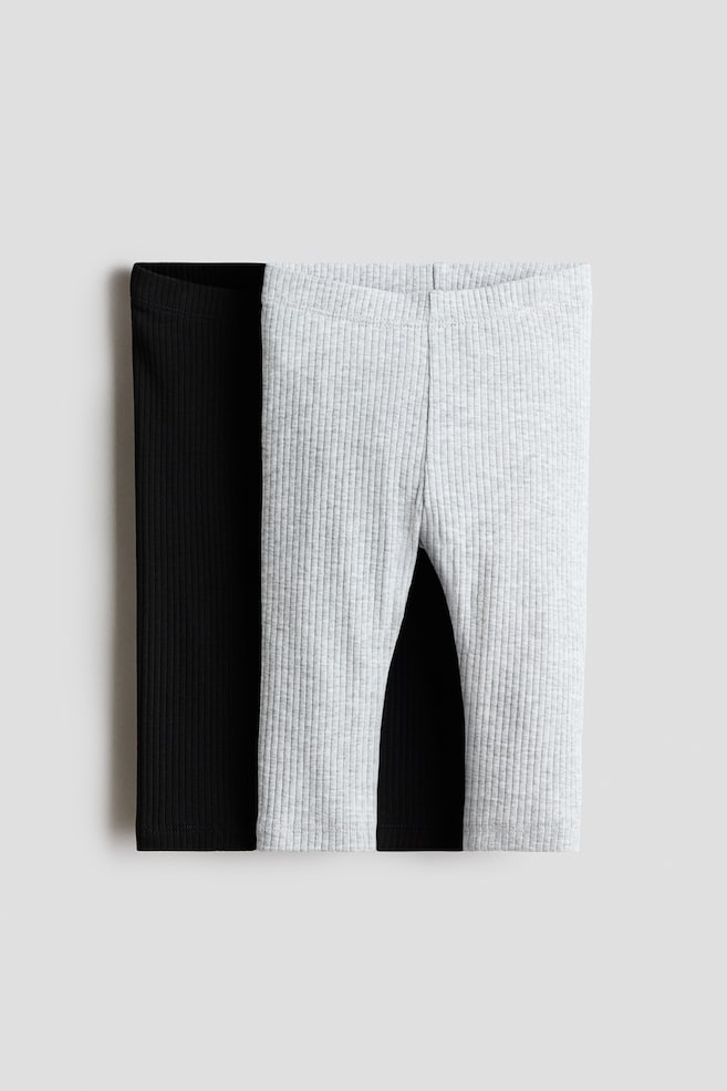 Two pairs of ribbed cotton jersey leggings are shown front on, with a light grey pair layered directly over a solid black pair. Both pairs feature an elasticated waistband, a vertical ribbed texture, and stitched ankle cuffs. - 1