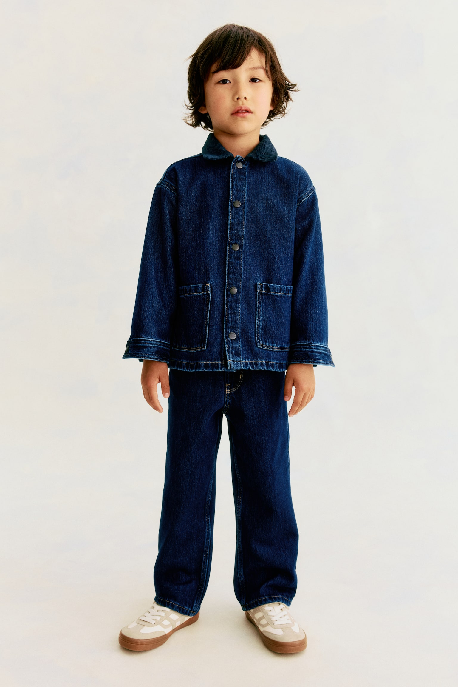 Dunkelblaue Denim-Jeans liegen flach und zeigen eine Vorderansicht. Sie verfügen über einen goldfarbenen Knopf, Gürtelschlaufen, zwei Vordertaschen und zwei kleine Münztaschen, wobei die Details durch eine kontrastierende, hellbraune Naht hervorgehoben werden. - 1