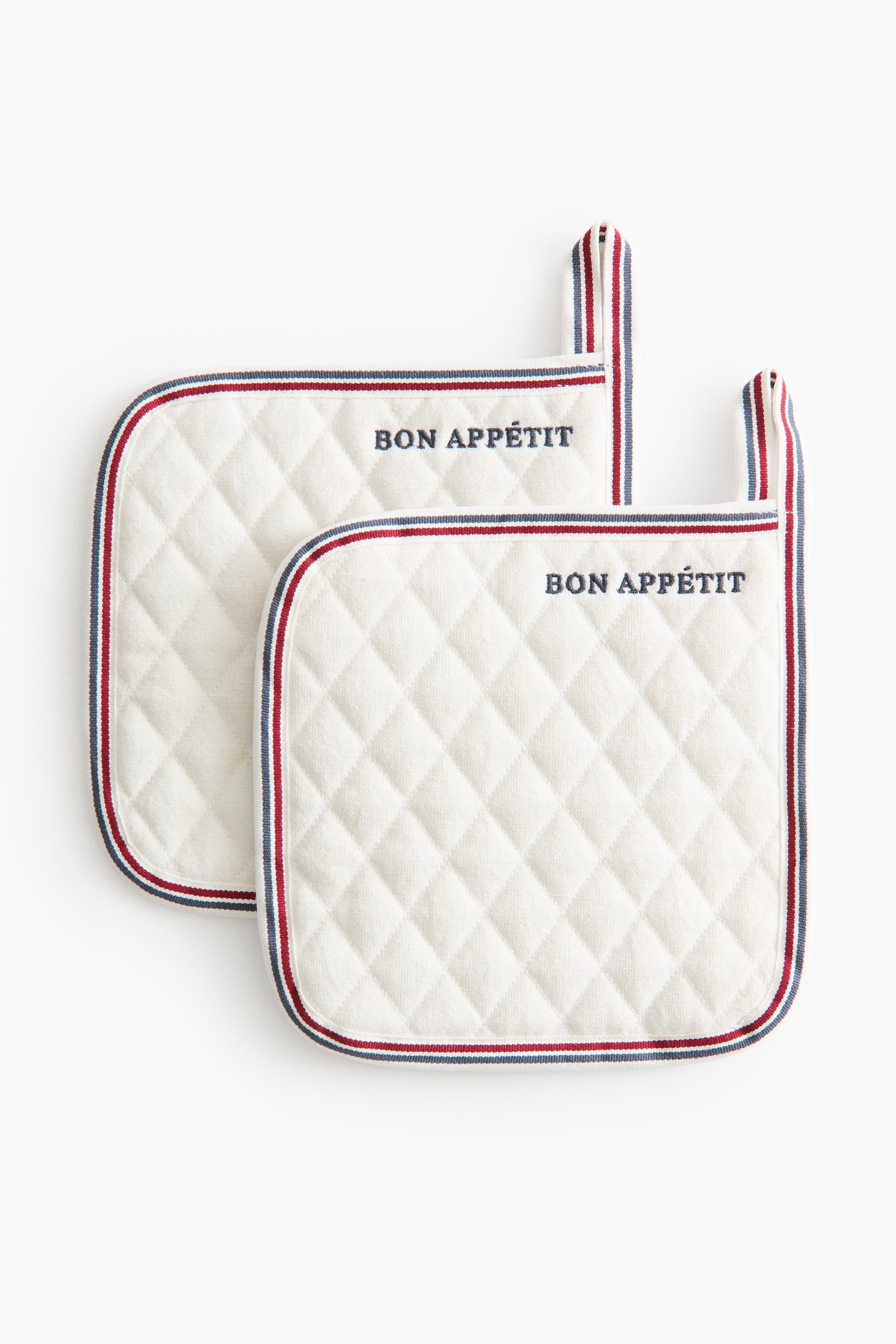 View larger image: Two off-white quilted pot holders are overlapping, both displaying a diamond pattern and featuring dark blue "BON APPÉTIT" text. They are bordered with a red, white, and blue striped fabric, and each presents a matching hanging loop at the top.