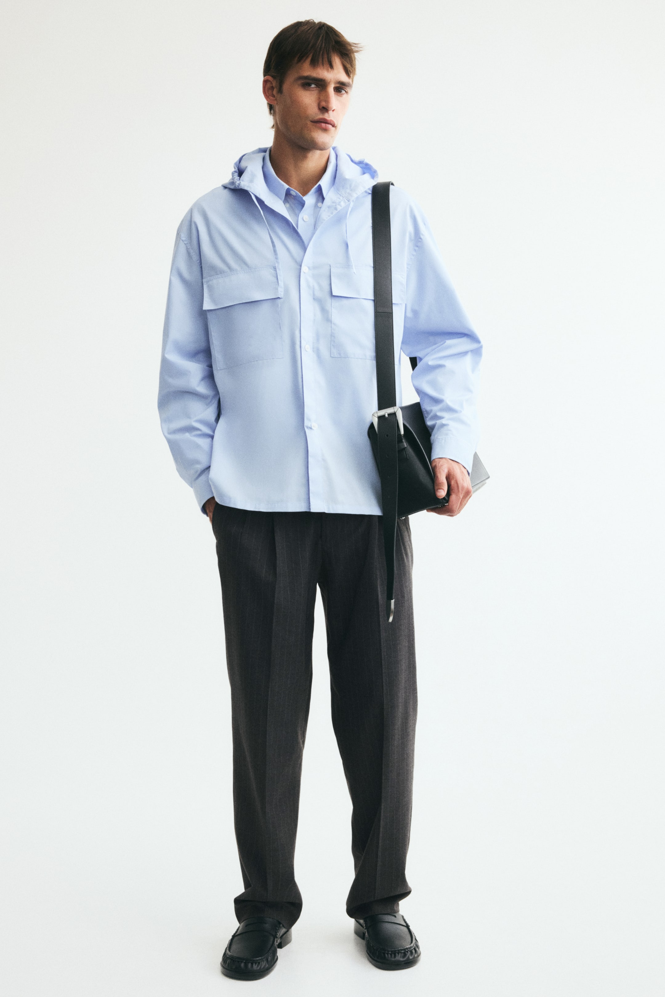 View larger image: Dark grey pinstriped suit trousers in woven fabric are worn by the model, featuring a regular fit, straight legs with front and back creases, and diagonal side pockets, with one hand resting in a pocket.