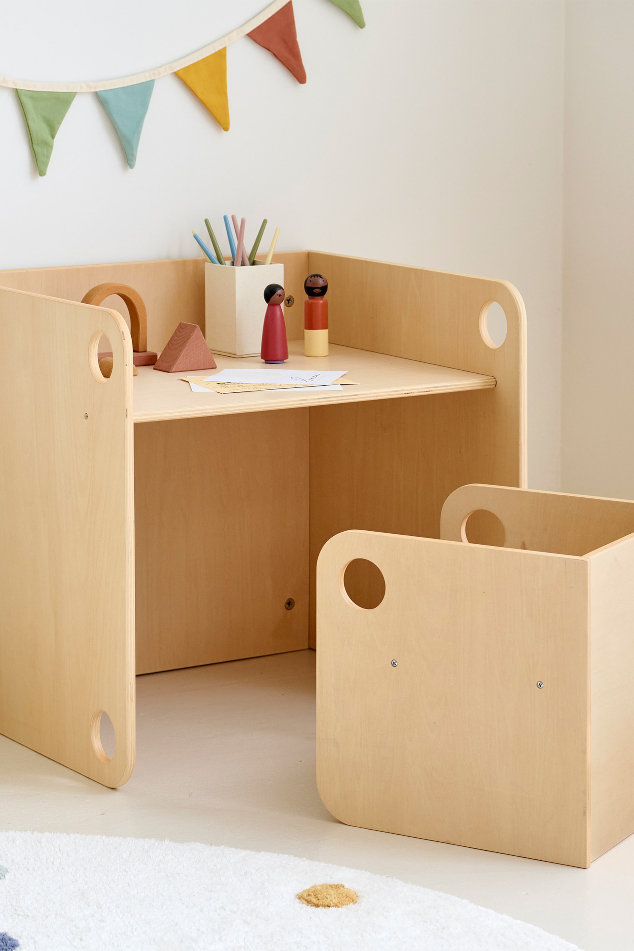 Größeres Bild ansehen: Ein Kinder-Schreibtisch aus hellem Holz und eine dazu passende offene Aufbewahrungsbox präsentieren ihr Design. Der Schreibtisch zeigt seine Oberseite und die rechte Seite mit abgerundeten Ecken und kreisförmigen Ausschnitten an den Seitenwänden. Die Aufbewahrungsbox zeigt ihre Vorder- und rechte Seite mit passenden abgerundeten Ecken und kreisförmigen Ausschnitten, die neben dem Schreibtisch positioniert ist.