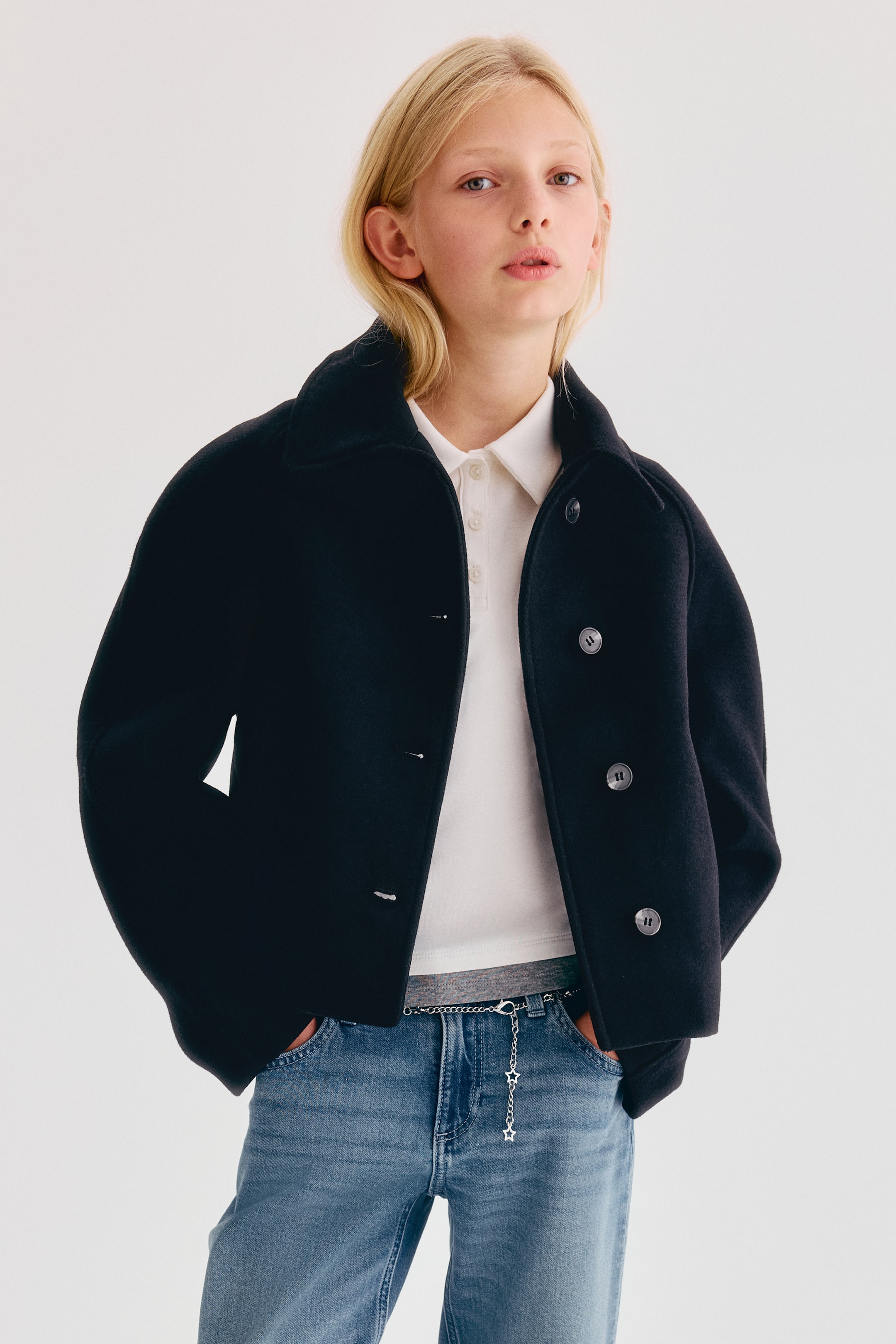 Größeres Bild anzeigen: Eine schwarze Jacke aus Filzstoff wird von vorne getragen und verfügt über einen breiten Kragen, Raglanärmel und große Frontknöpfe. Die Jacke ist offen über einem weißen Poloshirt gestylt, um ihre lässige Passform zur Geltung zu bringen.