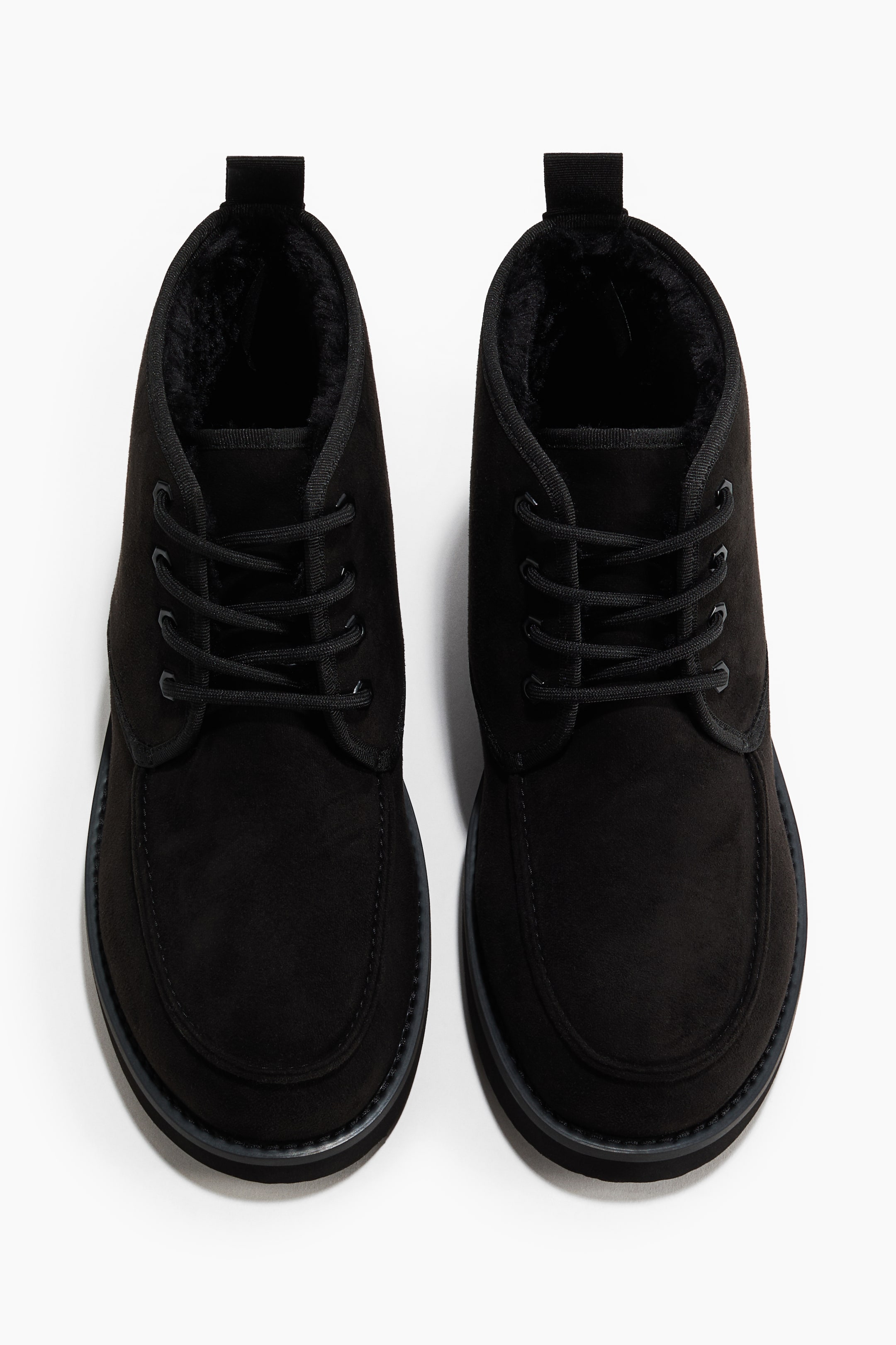 Visa större bild: Två svarta ankelboots i mocka visar sina snörfronter, med moc-toe-design och ett mjukt svart foder i fuskpäls. Varje stövel har också en svart dragflik baktill vid kragen och en tjock sula.
