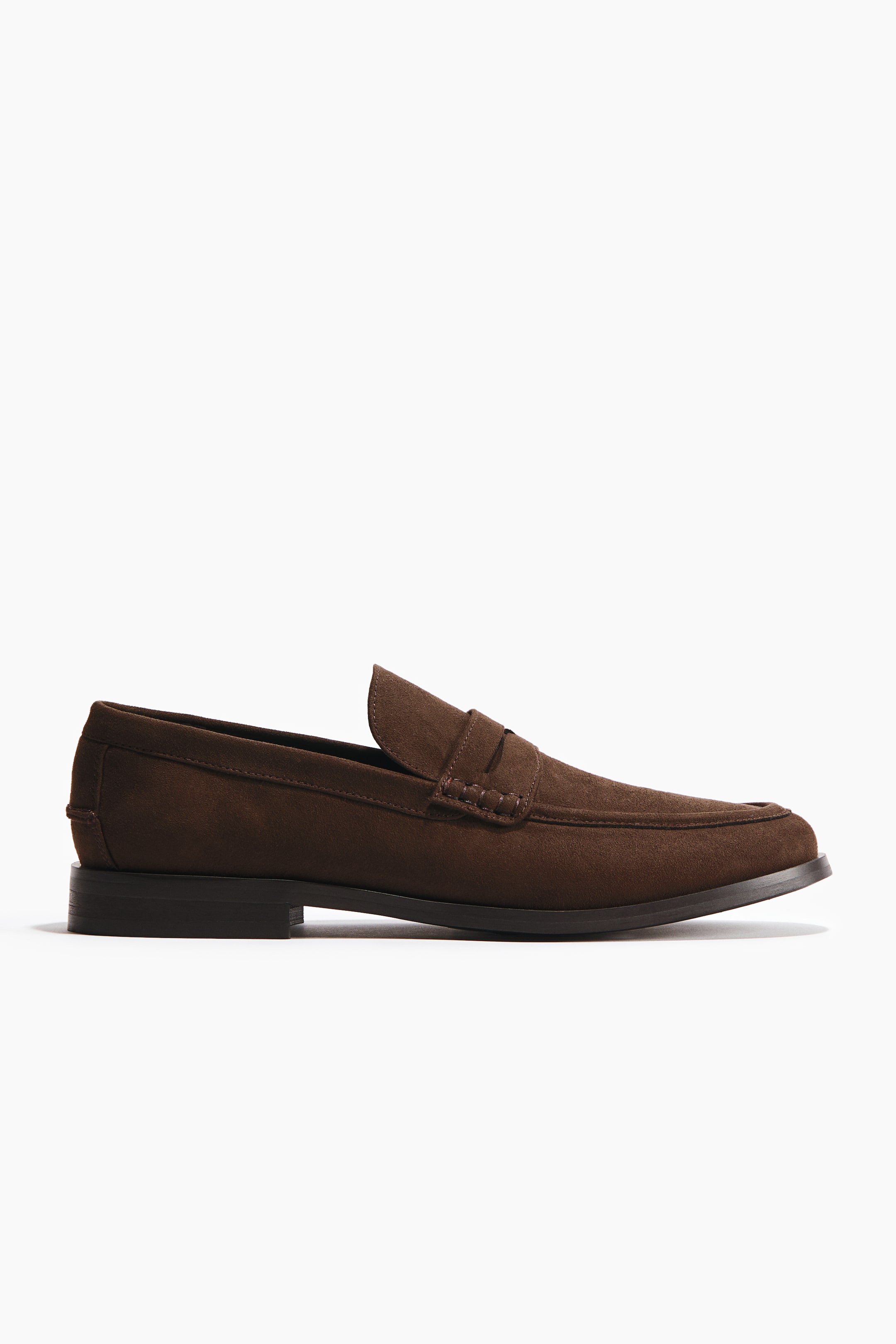 Grotere afbeelding bekijken: Een donkerbruine suède loafer wordt in zijaanzicht getoond, met een penny strap over de wreef, zichtbare stiknaden en een lage, donkere hak.