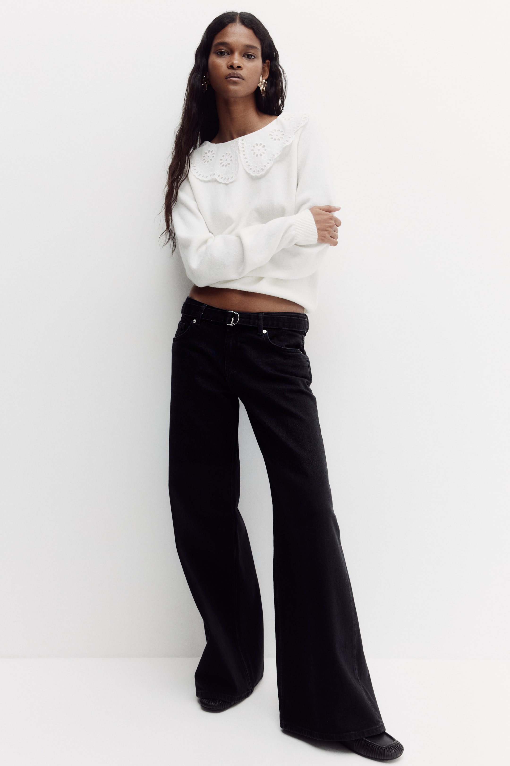 Ampliar la imagen: La modelo lleva puestos unos jeans negros de mezclilla de pierna ancha, con talle extra alto y corte amplio desde el muslo hasta el dobladillo. Un cinturón negro con hebilla en D plateada ciñe la cintura, y los jeans llegan hasta la parte superior de los pies de la modelo.