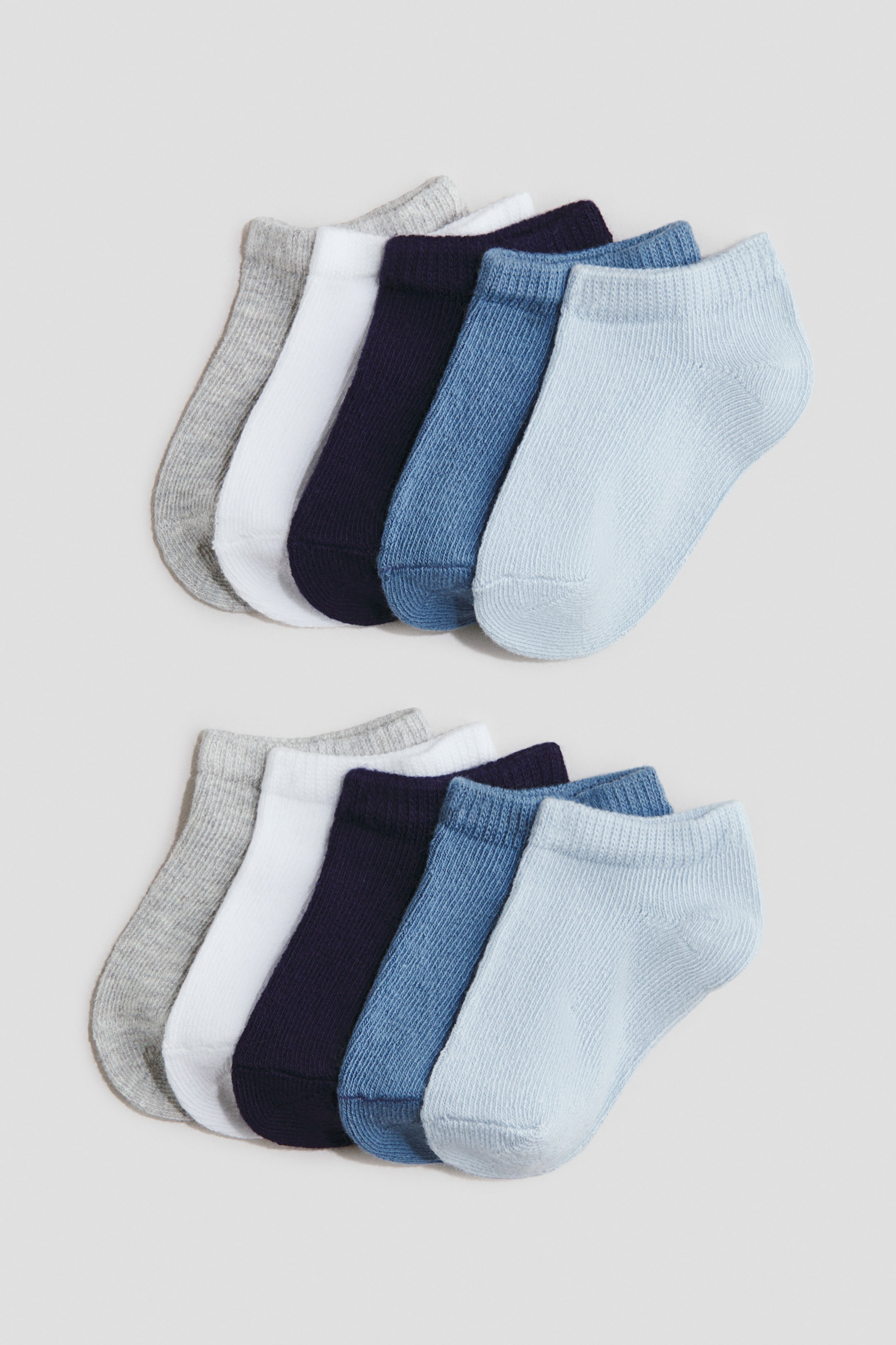 View larger image: Shaftless socks are displayed in two fanned-out rows, with each row showcasing five socks facing forward. Each sock boasts a soft, fine-knit texture with ribbed cuffs, and the colors transition from gray, white, navy, medium blue, to light blue.