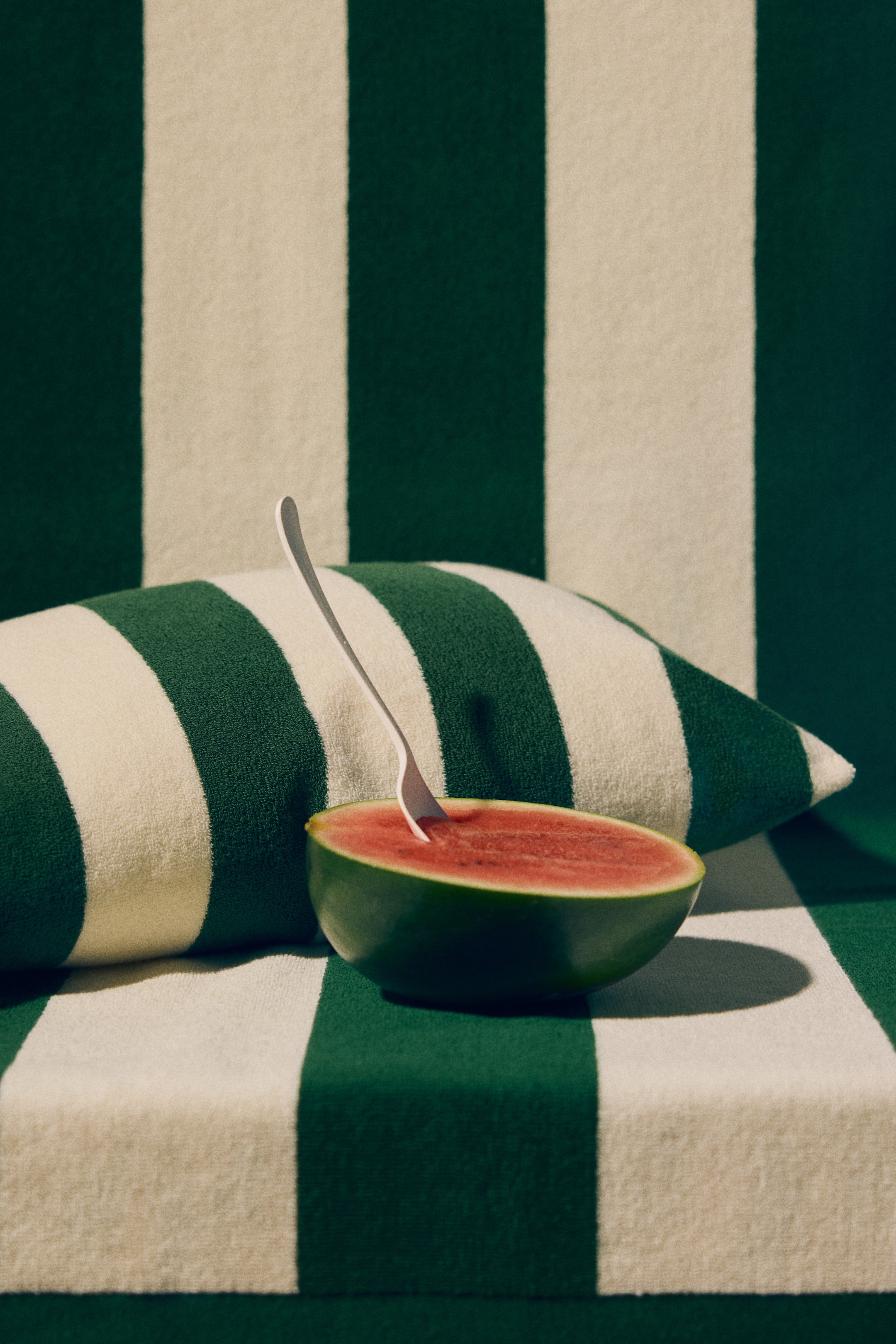View larger image: A halved watermelon showcases its deep green rind and bright red flesh, dotted with a few small black seeds. A silver fork stands upright in the red flesh.