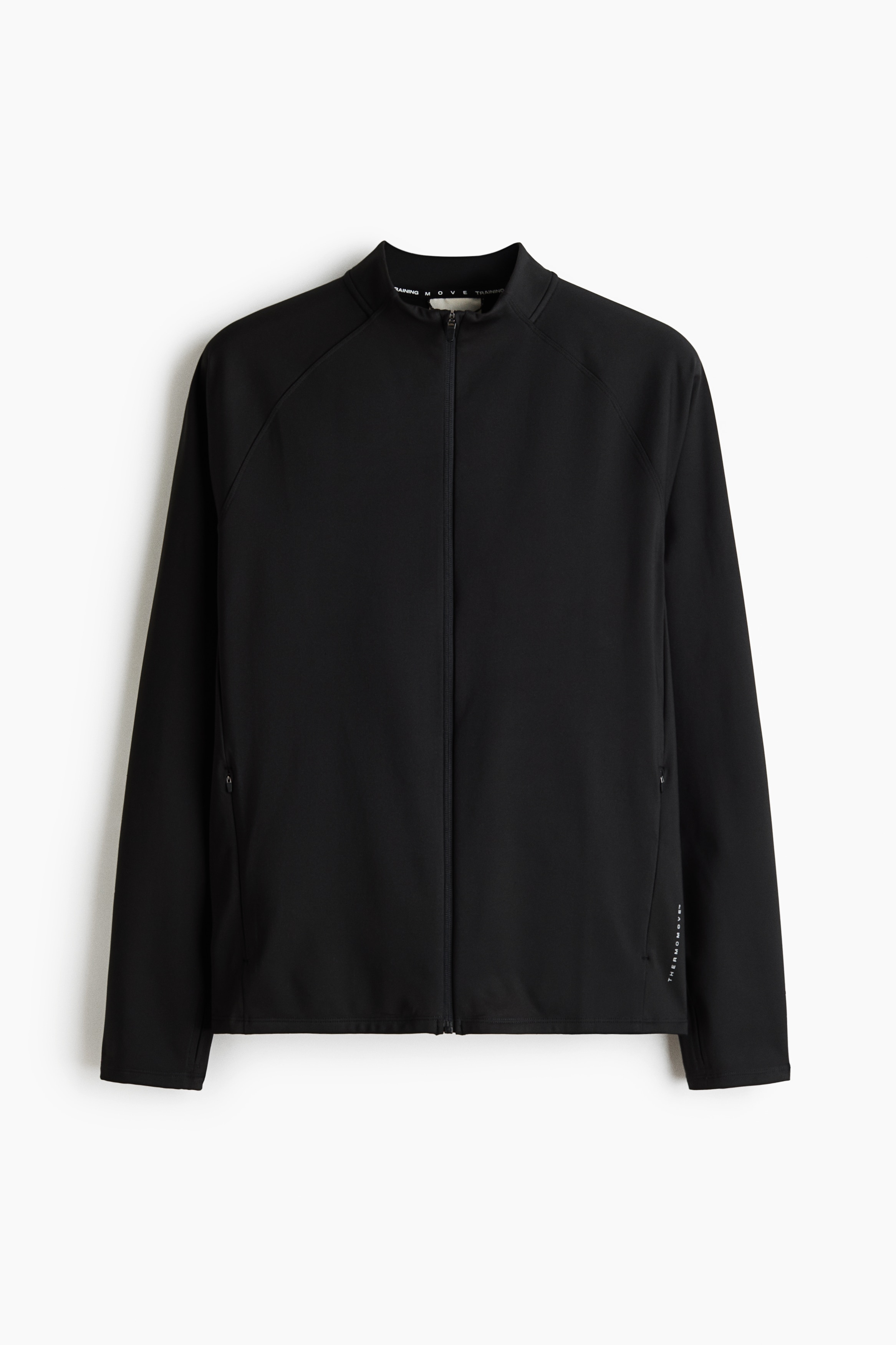 A black, long-sleeved athletic jacket with a zippered front and thumbholes is being worn by the model. The jacket is styled with a grey neck gaiter, dark grey shorts layered over black leggings, and grey athletic shoes.