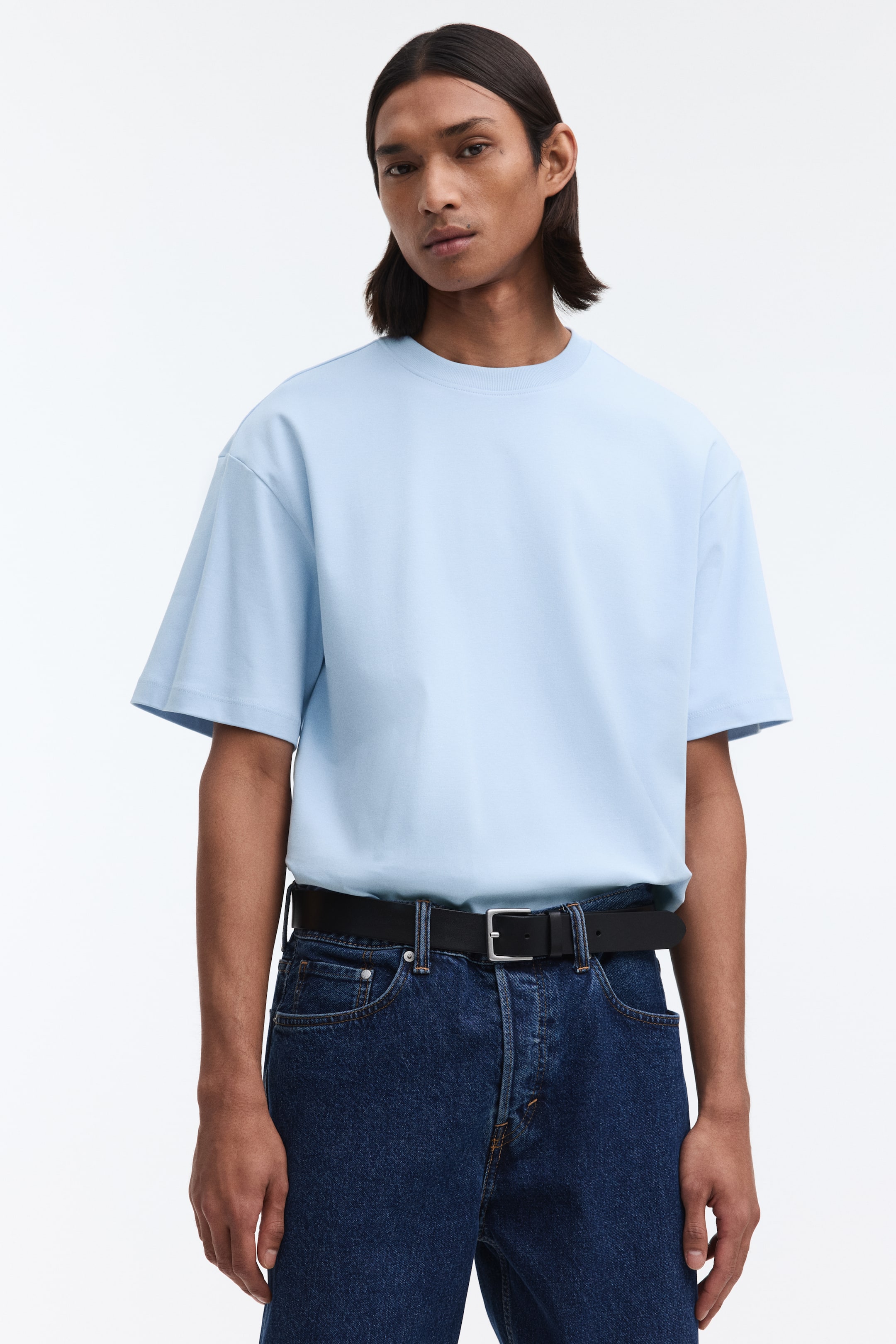 Ampliar la imagen: Una camiseta azul claro de cuello redondo está orientada hacia adelante, con un ajuste holgado que presenta hombros caídos y mangas cortas sueltas. Se lleva metida en la cintura, presentando una silueta definida.