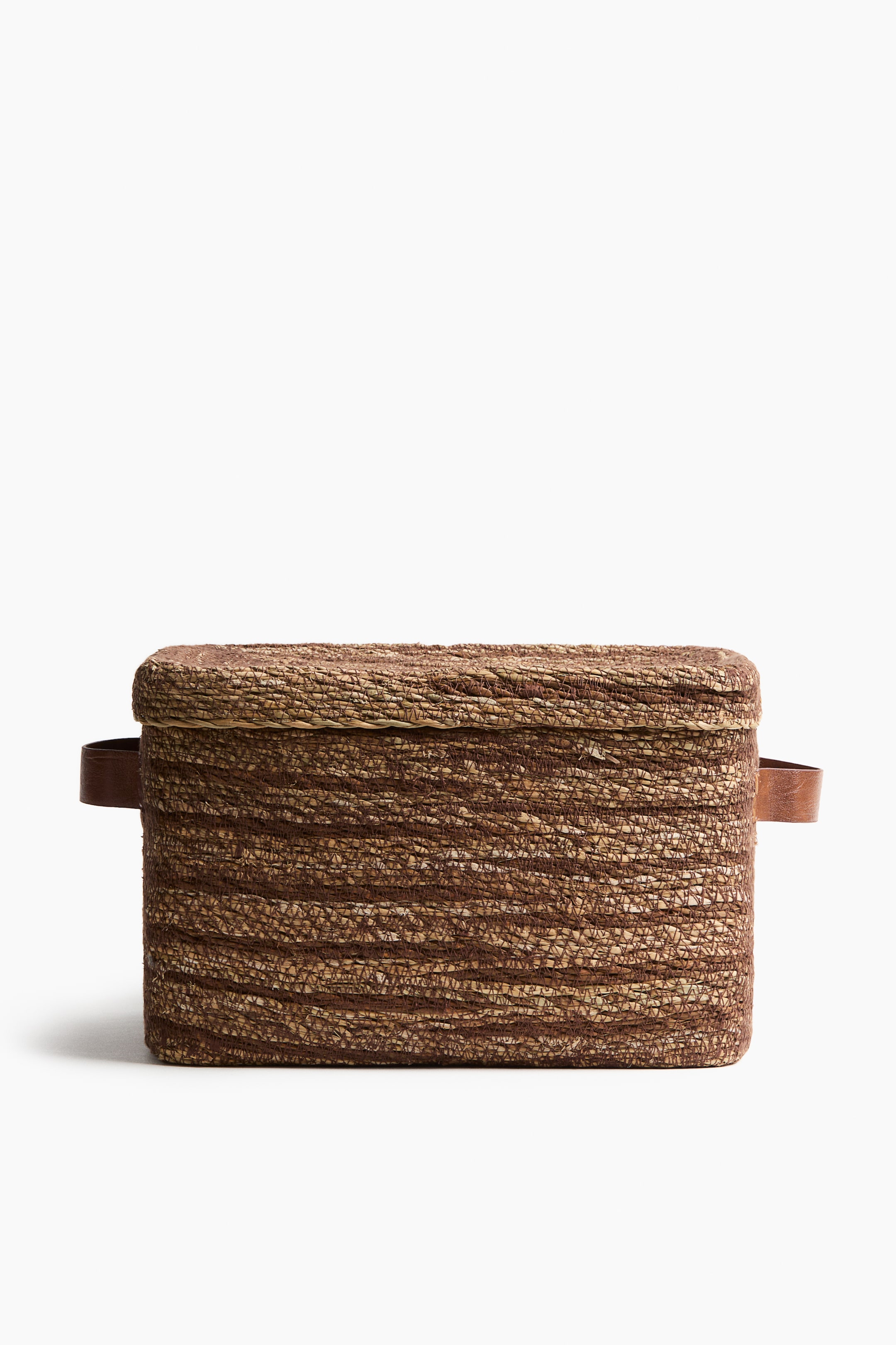 View larger image: A rectangular storage basket showcasing a braided seagrass construction in shades of brown and tan. A matching lid covers its top, with coated brown handles extending from its shorter sides.