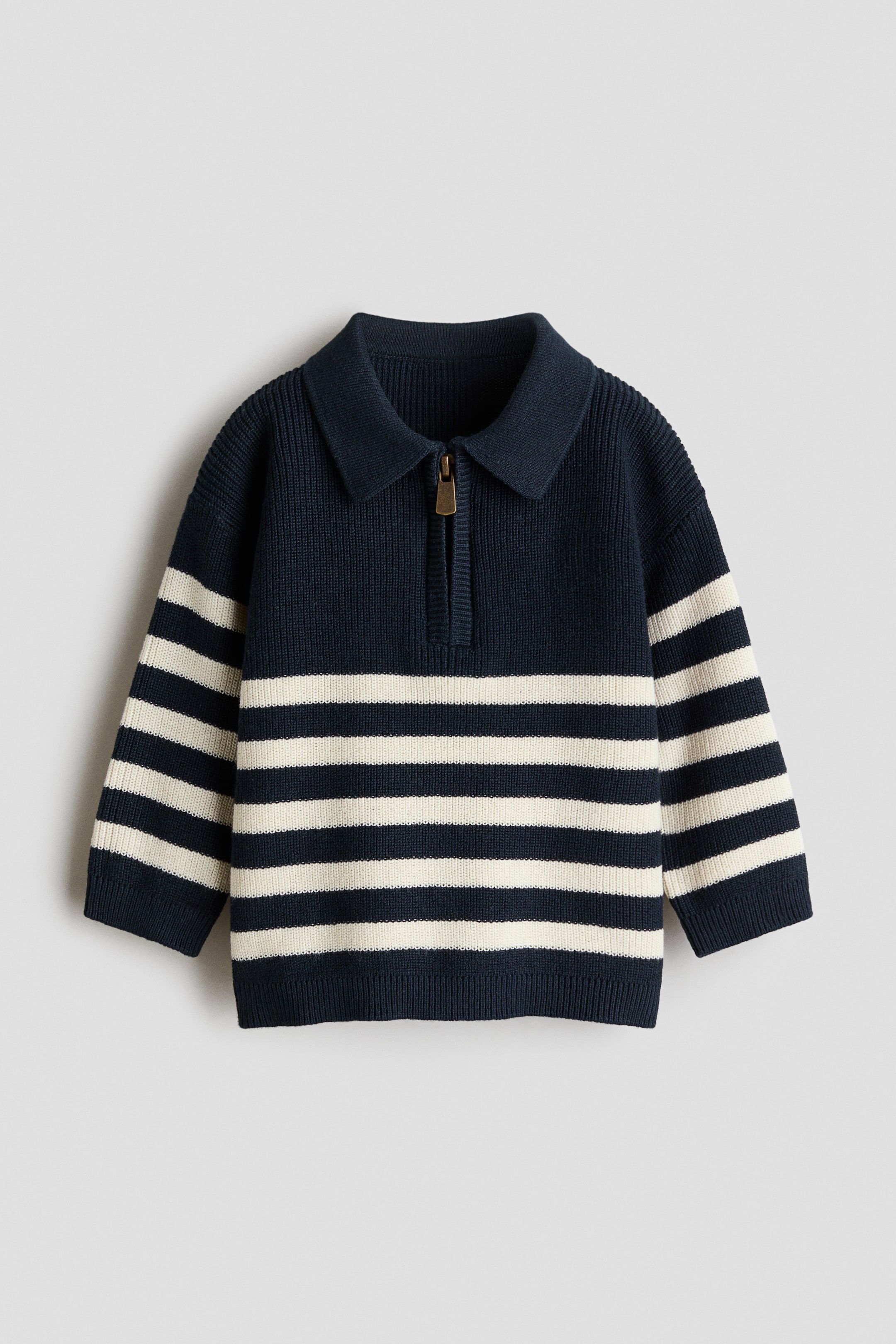 View larger image: The baby's sweater is shown from the front, highlighting a navy blue ribbed knit upper body with a polo collar and a quarter-zip placket. The placket is secured with a gold-tone zipper pull, and the long sleeves and lower body feature horizontal off-white stripes set against a navy background.