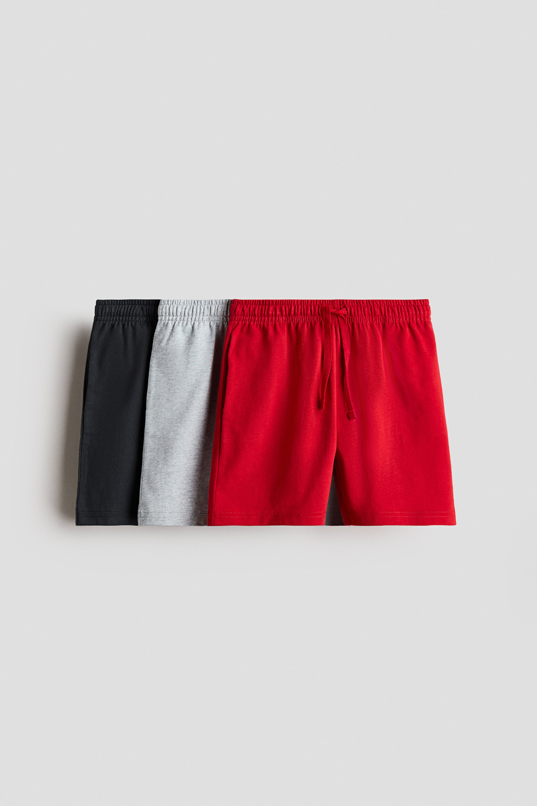 View larger image: Three pairs of soft cotton jersey shorts are arranged side-by-side, displaying their front view, in black, light grey, and red. Each pair is designed with an elasticated drawstring waist, with the drawstring on the red shorts clearly visible and tied.