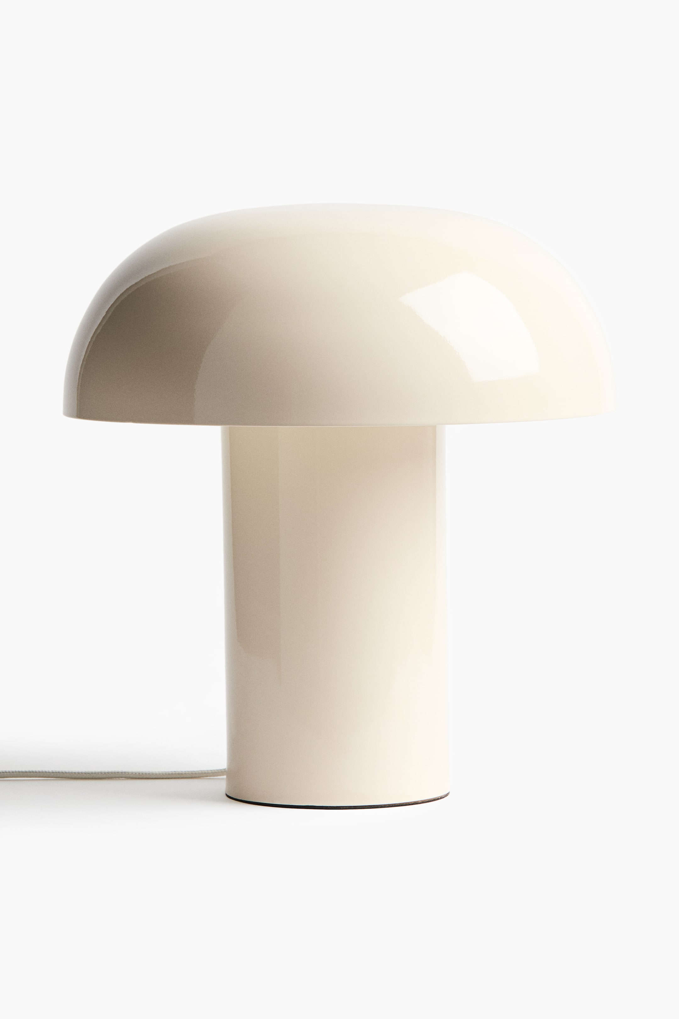 Visa större bild: En krämfärgad svampformad bordslampa presenteras framifrån, med en glansig kupolformad skärm ovanpå en cylindrisk bas. En ljusgrå flätad strömkabel sträcker sig från basens baksida.