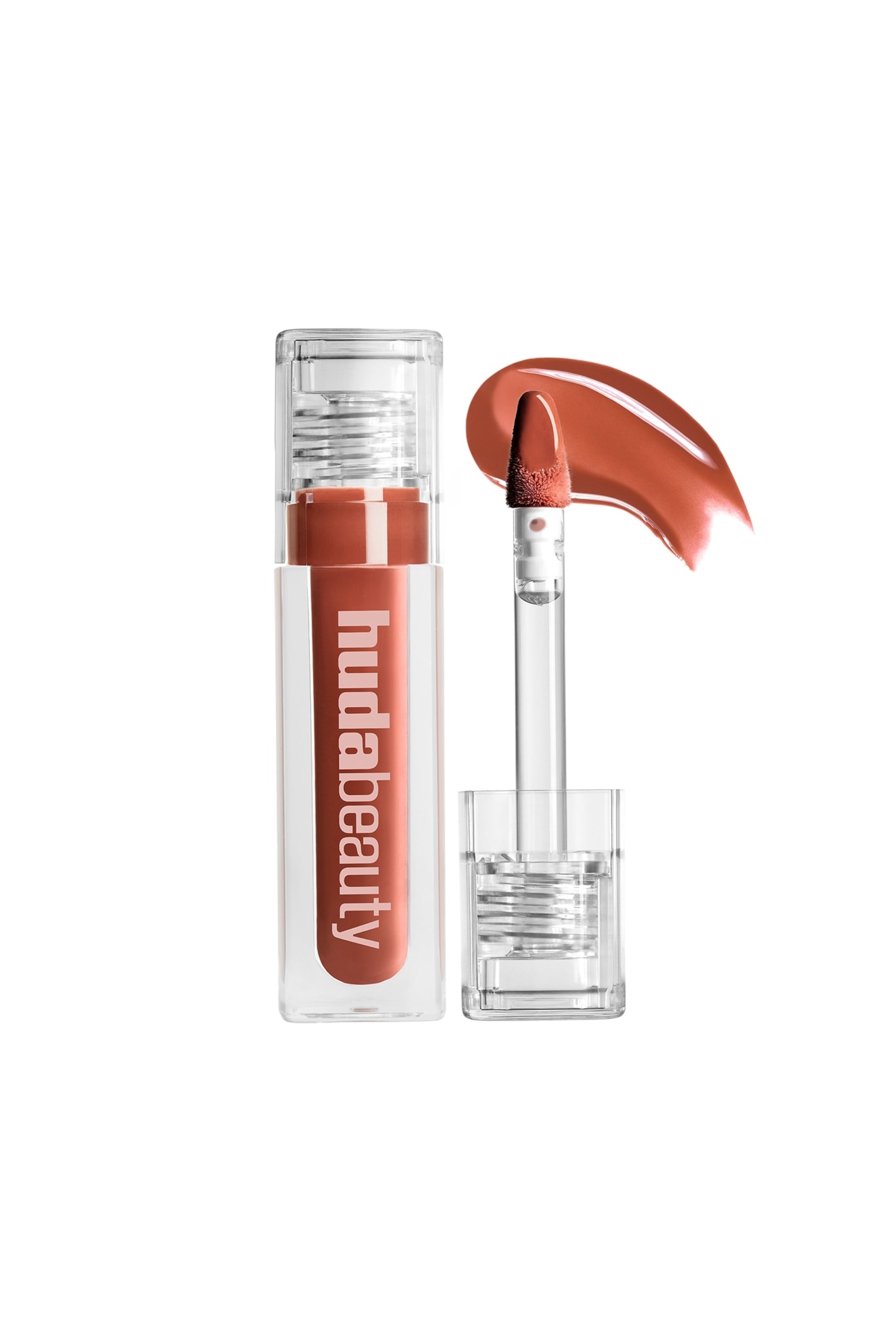 Vis større bilde: En klar, rektangulær lipgloss-tube står oppreist, inneholder en rødbrun gloss og viser 'hudabeauty' vertikalt. En applikator med doe-foot er vist trukket ut fra tuben og står ved siden av, dekket med samme gloss, med en buet stripe av produktet også synlig.