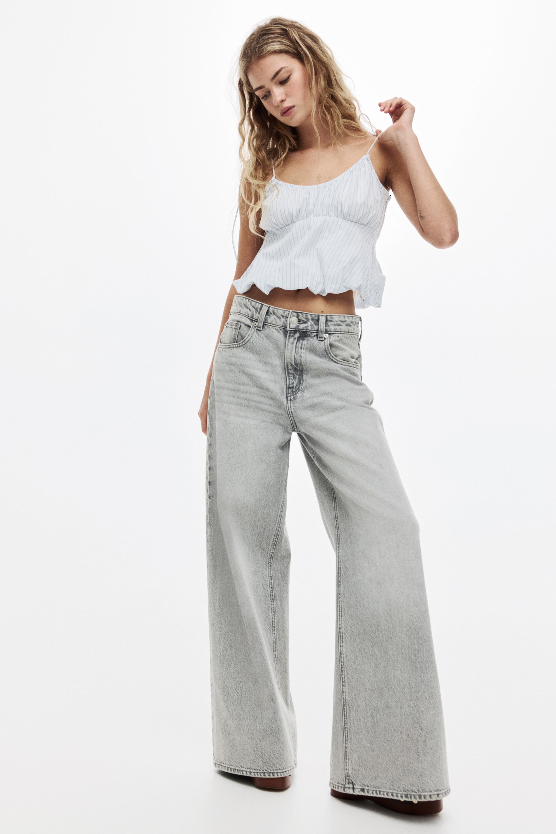 Ampliar la imagen: Los jeans son de mezclilla de lavado claro, con un corte de cintura alta y pierna ancha, y el clásico diseño de cinco bolsillos, vistos desde un ángulo de frente. Se extienden hasta el suelo, mostrando una silueta de largo completo.