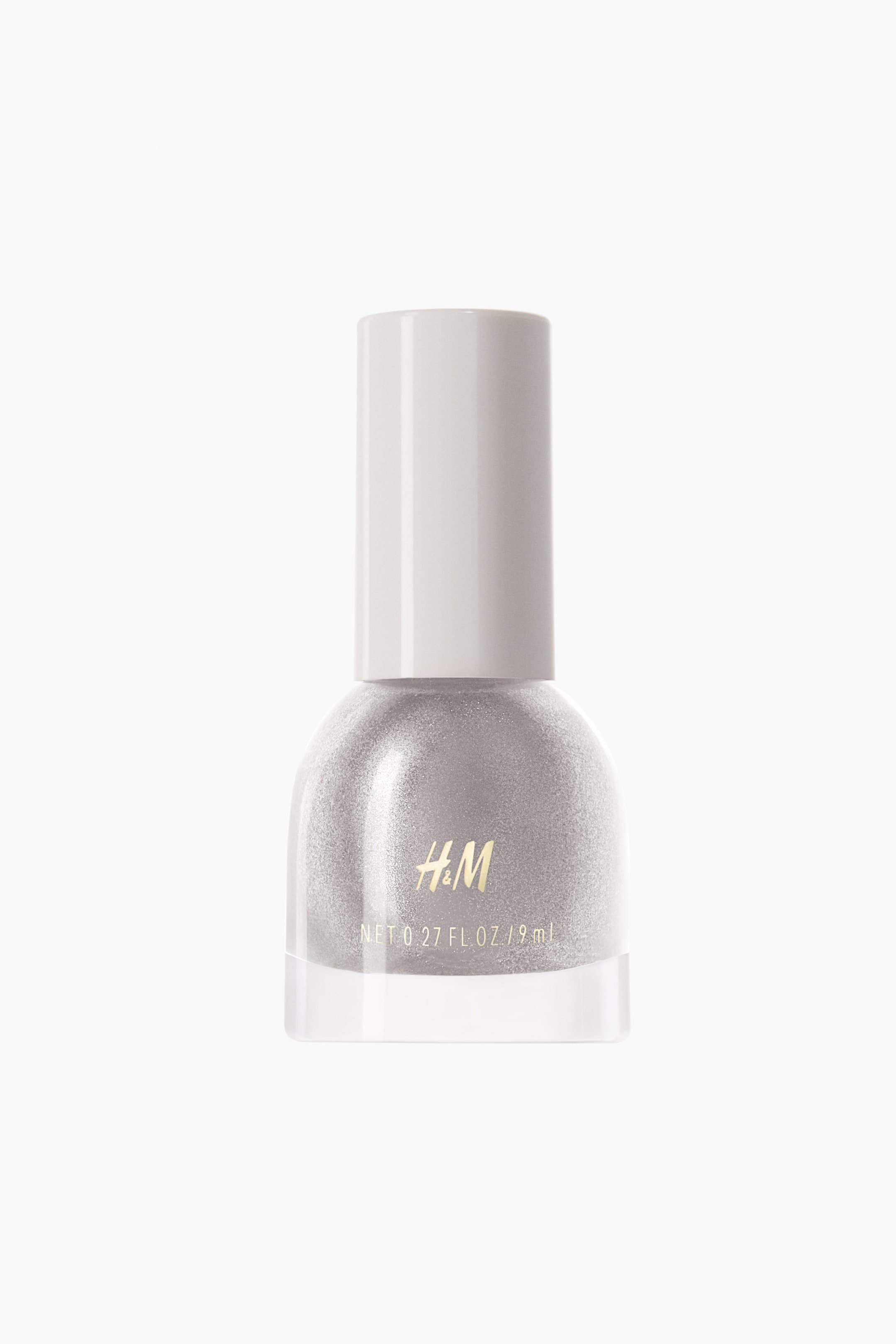 View larger image: A nail polish bottle is presenting a front view, featuring a light grey cylindrical cap. The clear glass bottle is holding shimmering light silver nail polish, with a gold "H&M" logo and volume details visible on its front surface.