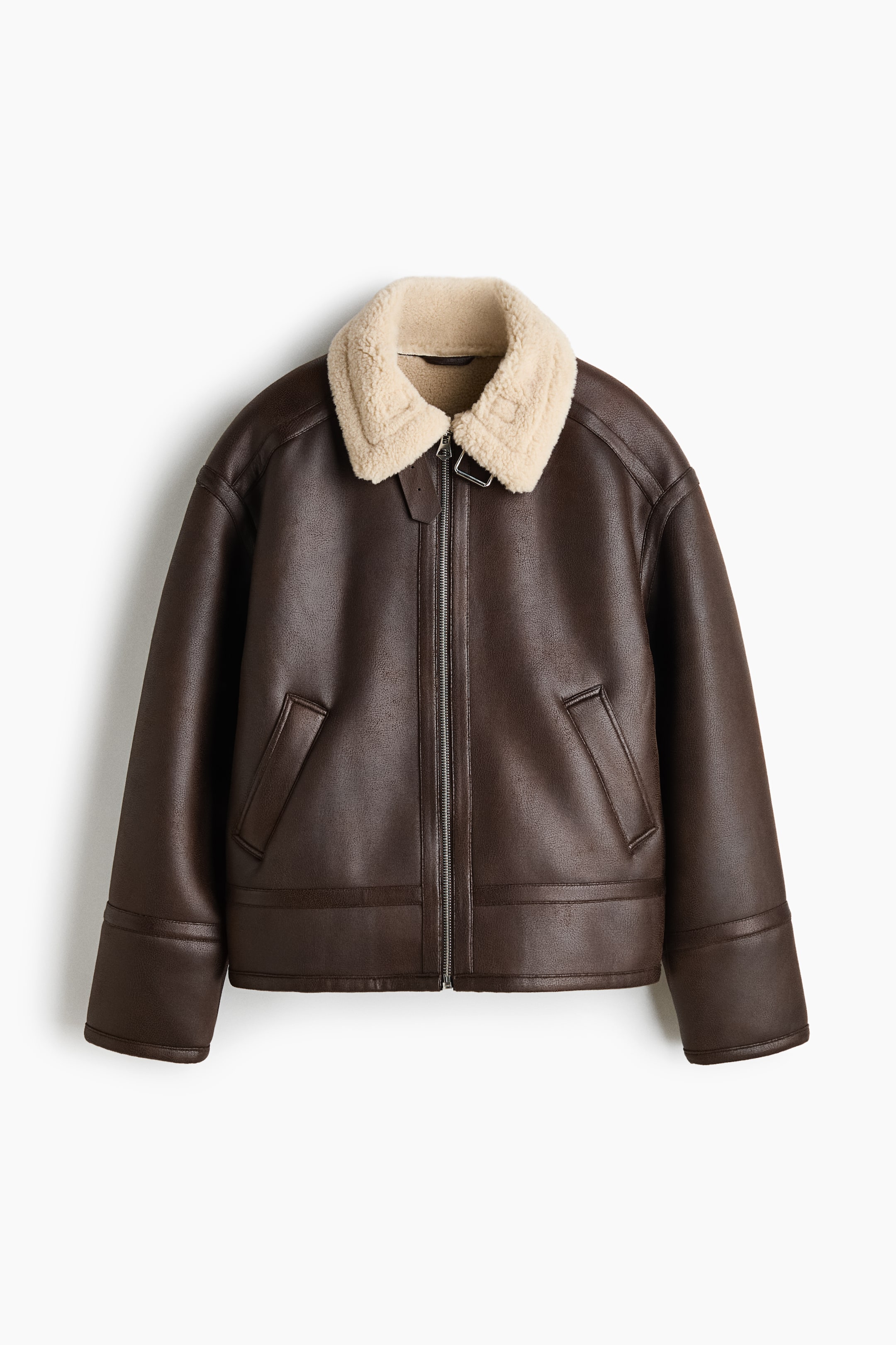 View larger image: A dark brown aviator jacket is shown from the front, featuring a contrasting cream shearling collar and a centre front zip closure. It features dropped shoulders, angled welt pockets, and wide stitched details at the cuffs and hem.