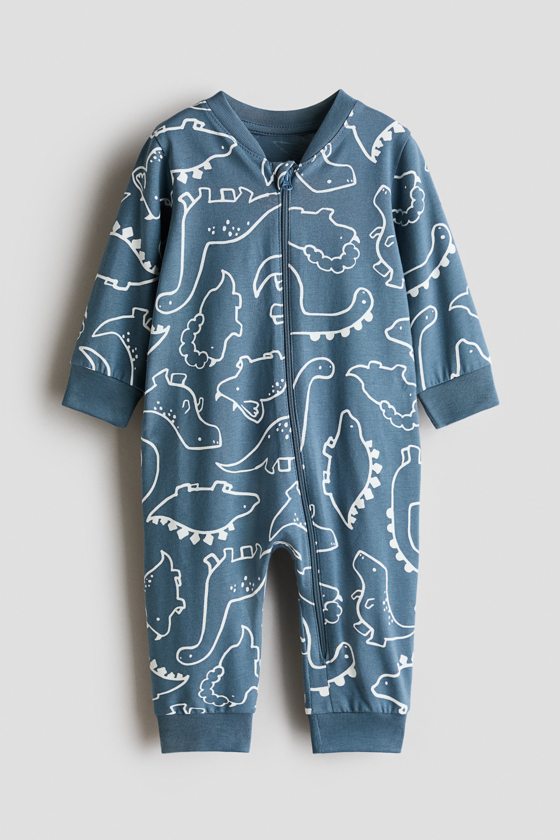 View larger image: A blue baby jumpsuit na may all-over white dinosaur outline print, dinisenyo na may full-length front zipper, ribbed crew neck, at ribbed cuffs sa mga manggas at bukong-bukong.